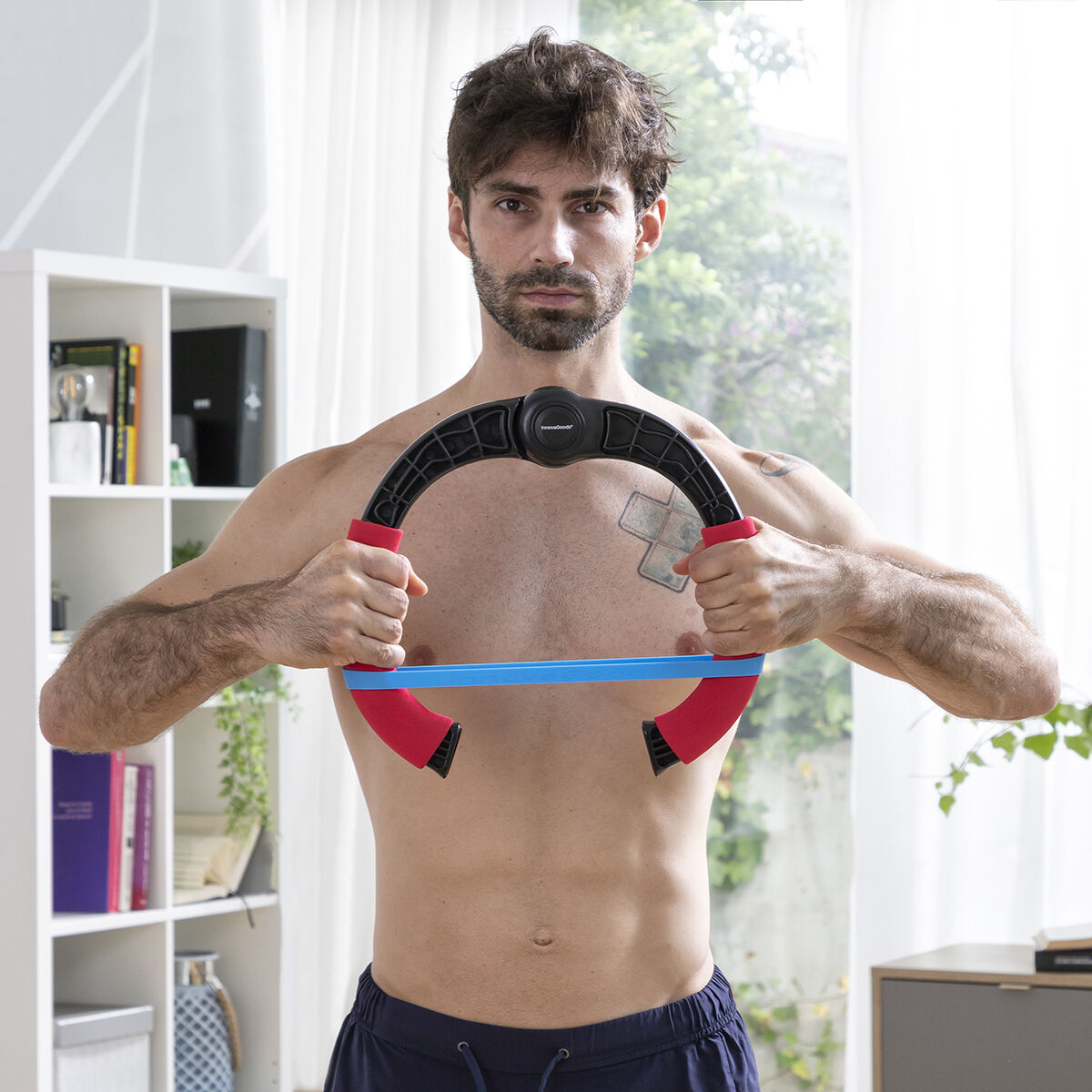 Mann hält Fitnessring vor sich. Er ist oberkörperfrei, mit Tätowierung auf der Brust.