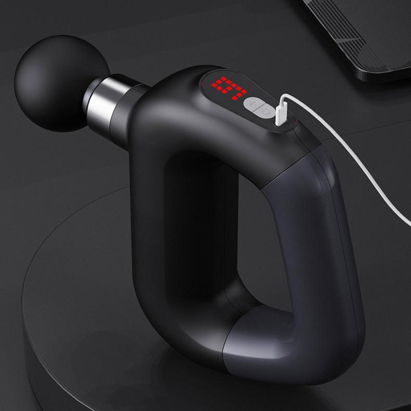 Schwarze Massagepistole mit roter Anzeige und Ladekabel. Das Gerät steht auf einer schwarzen Oberfläche. Freisteller.