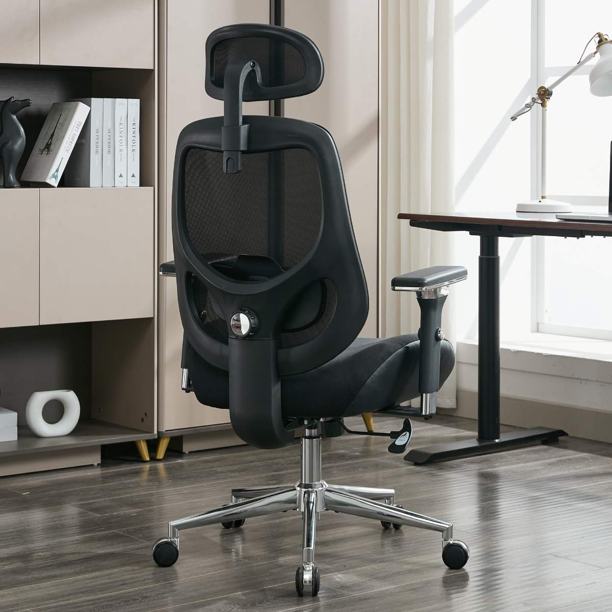 Ein schwarzer ergonomischer Bürostuhl steht vor einem Schreibtisch. Er hat eine Kopfstütze und Armlehnen.