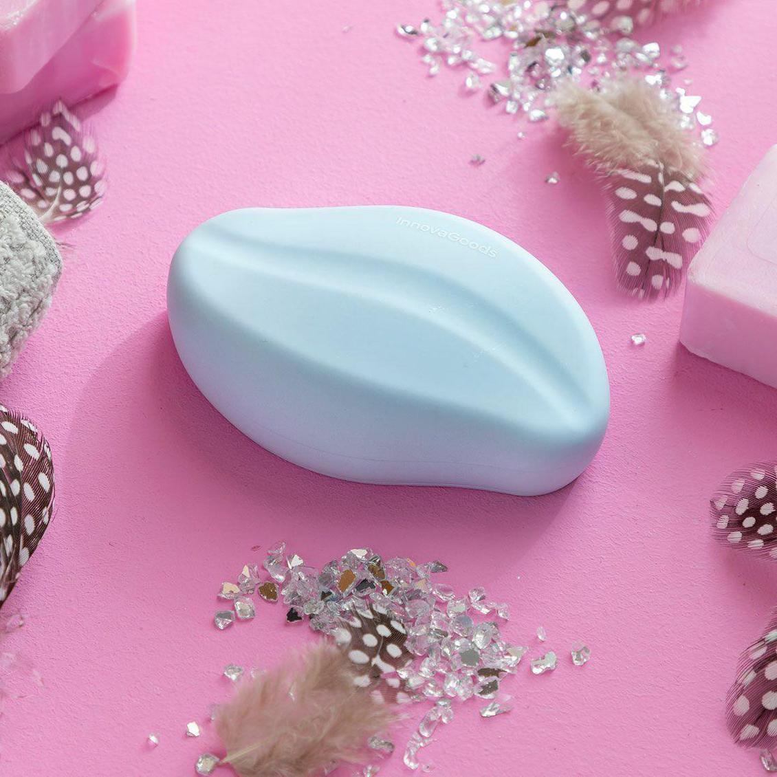 Un sapone blu ovale su una superficie rosa con piume, saponi e glitter sparsi.
