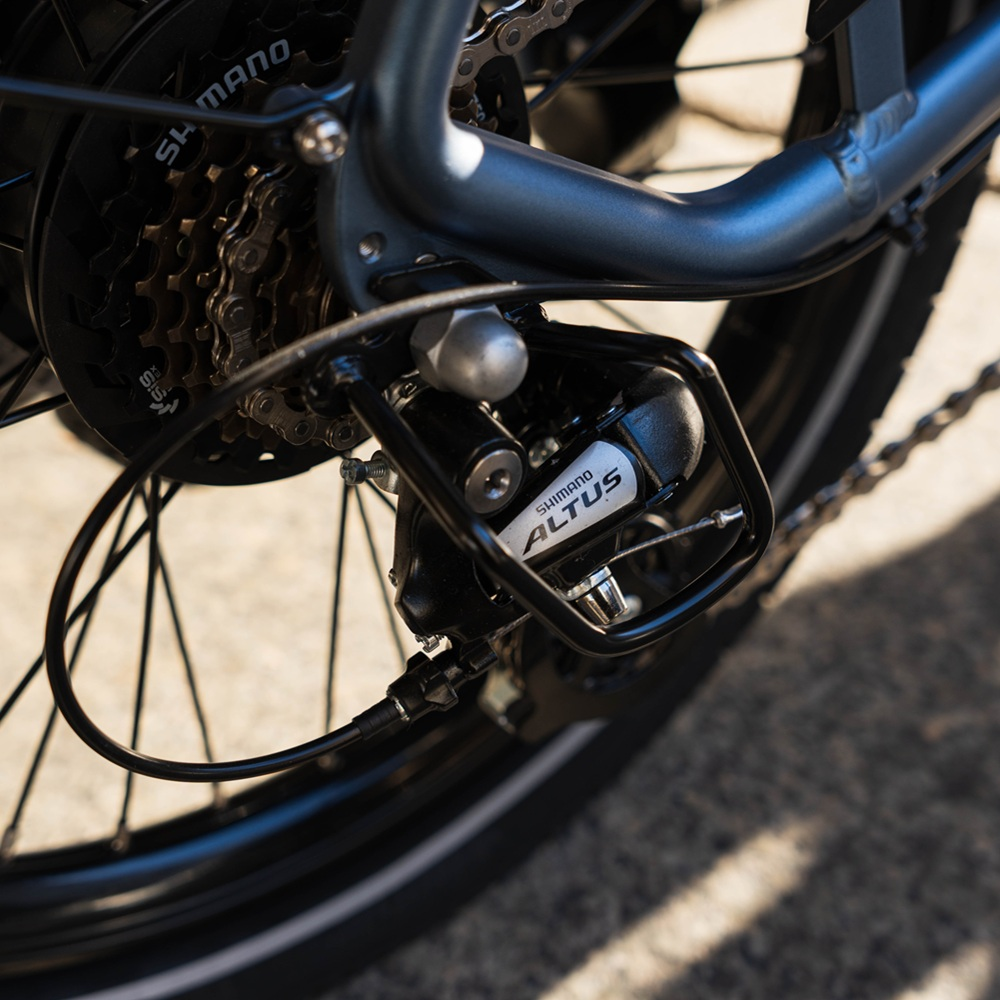 Primo piano di un deragliatore Shimano Altus su una bici. Lo sfondo è sfocato.