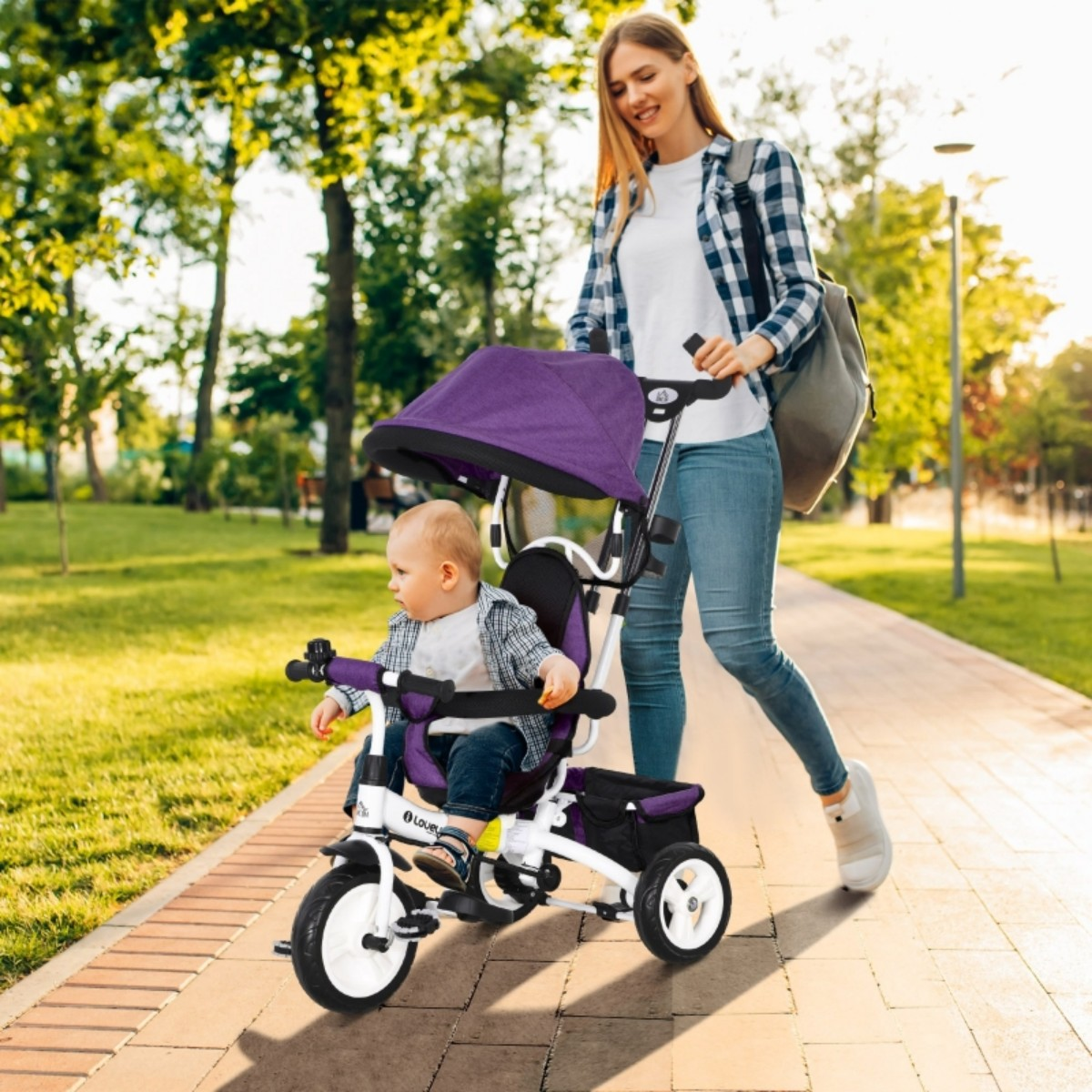 Eine Frau schiebt ein Dreirad mit einem Baby darin, draußen in einem Park.