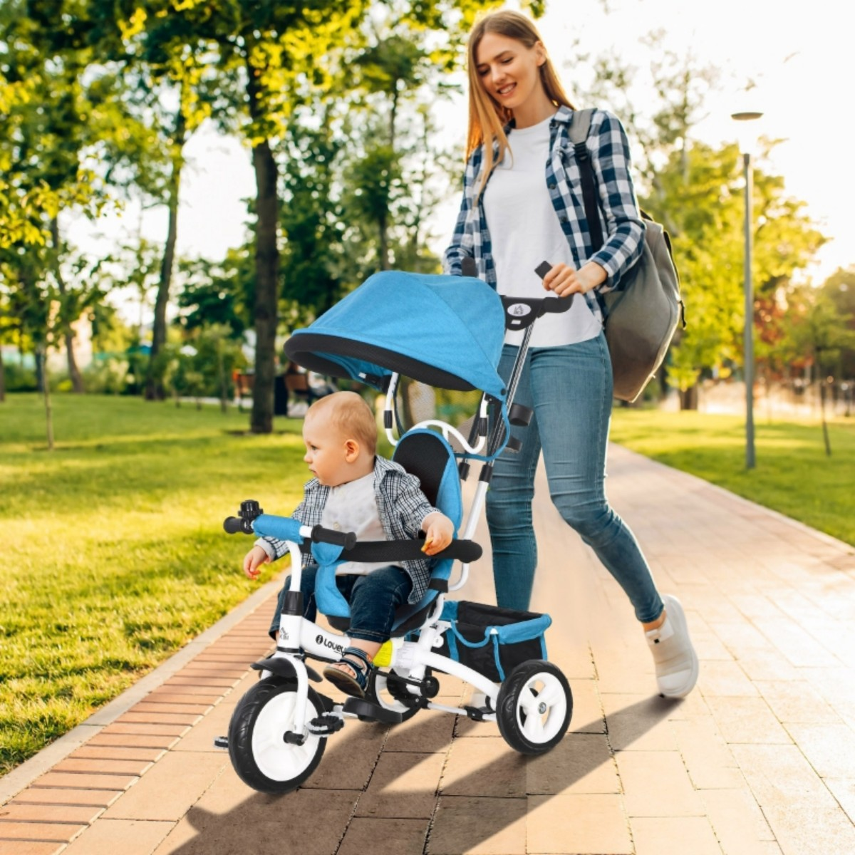 Eine Frau schiebt ein blaues Dreirad mit einem Baby, das darin fährt. Sie befinden sich an einem sonnigen Tag auf einem gepflasterten Weg im Park.