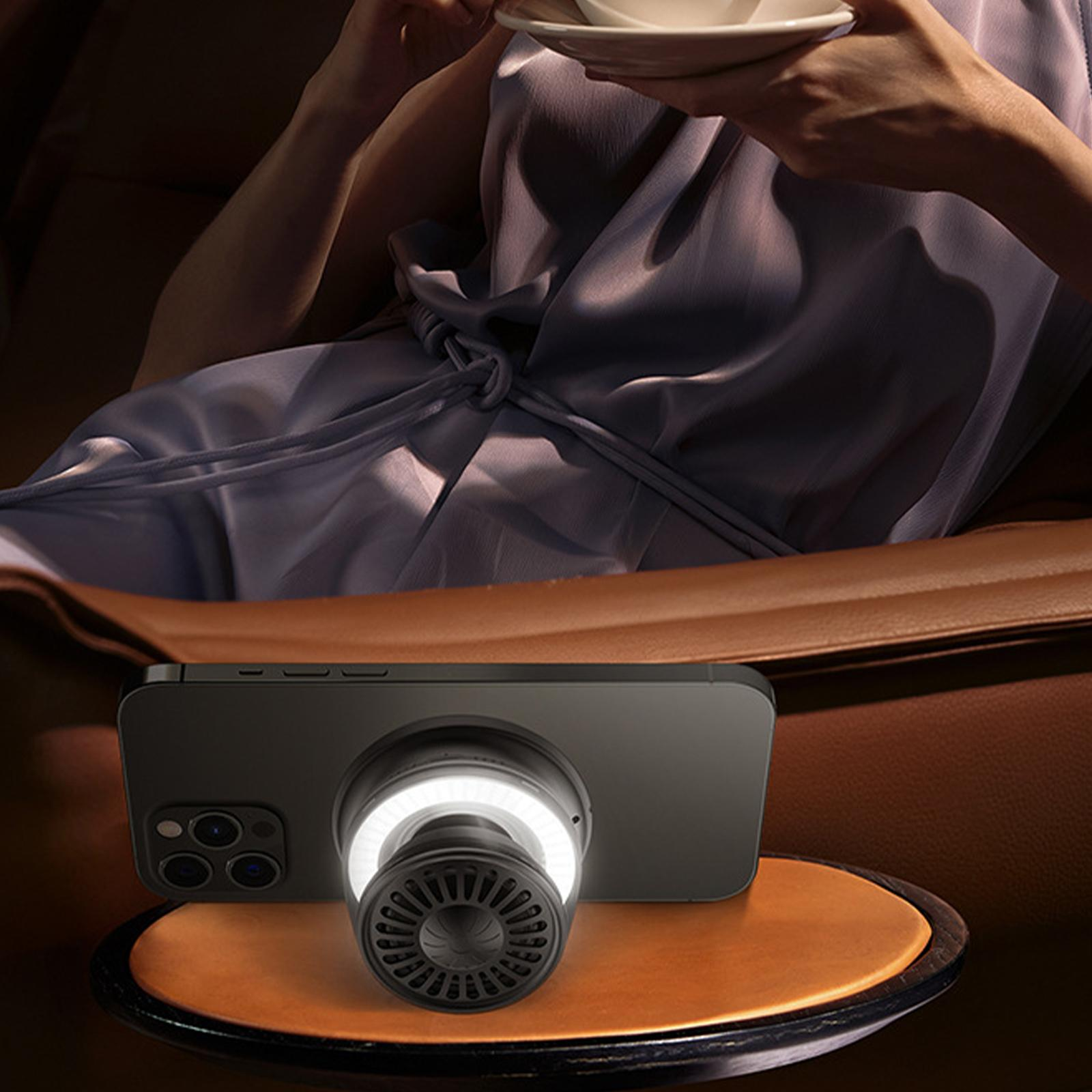 Ein schwarzes Smartphone mit einem Ringlicht, vor einer Person. Brauner Tisch.