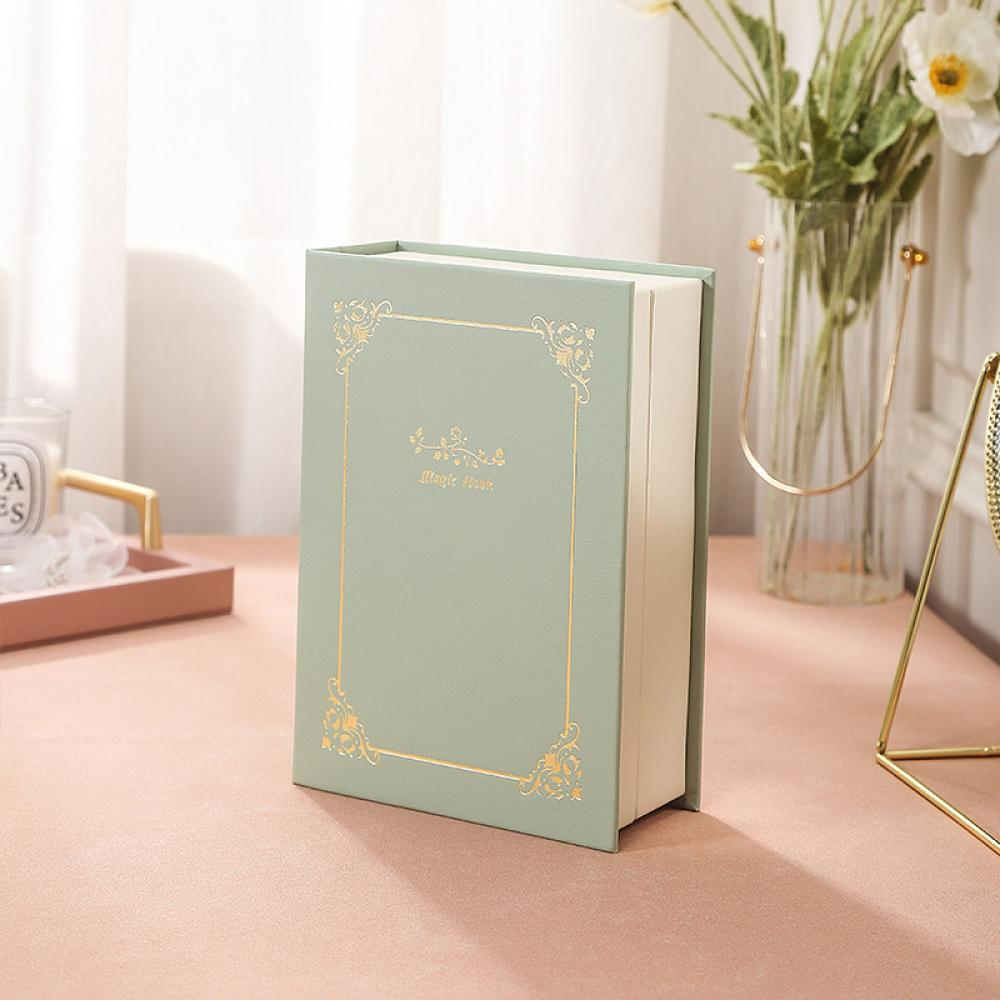Ein grünes Buch mit goldenem Rand und dem Text 'Magic Book' liegt auf einer rosa Oberfläche.