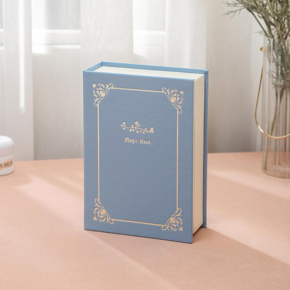 Ein blaues Buch mit goldenem Rand und dem Text 'Magic Book' liegt auf einer rosa Oberfläche.