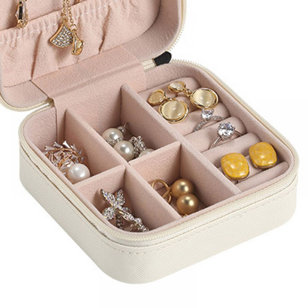 Offene Schmuckschatulle mit Fächern gefüllt mit Ringen, Ohrringen und Halsketten. Die Box ist beige und der Innenraum rosa.