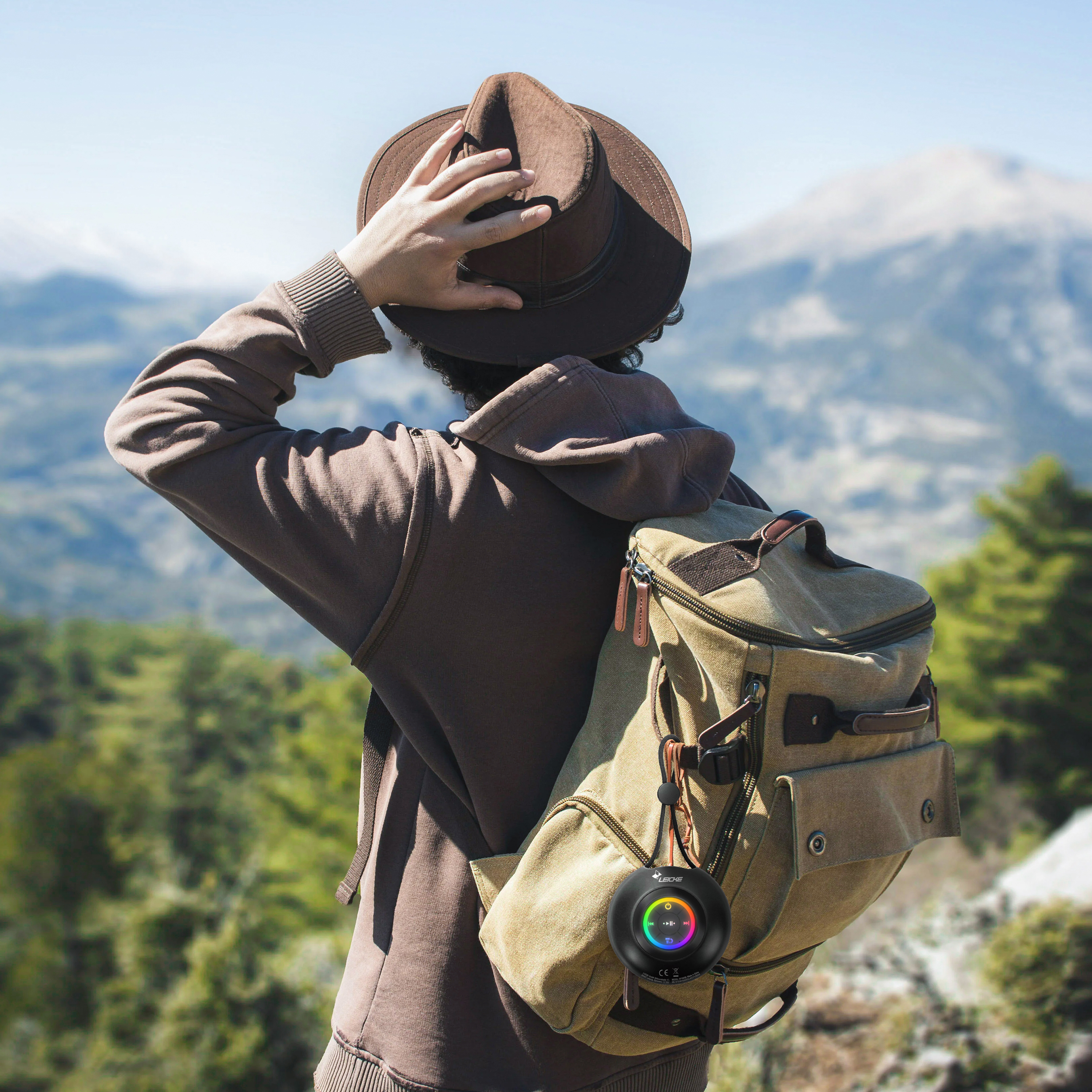 Una persona con cappello e zaino osserva un panorama montano. Un altoparlante è collegato allo zaino.