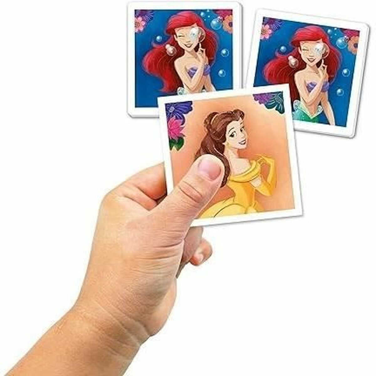 Mano che tiene tre carte di Disney Princess. Una mostra Ariel, un'altra Belle. Sfondo luminoso.