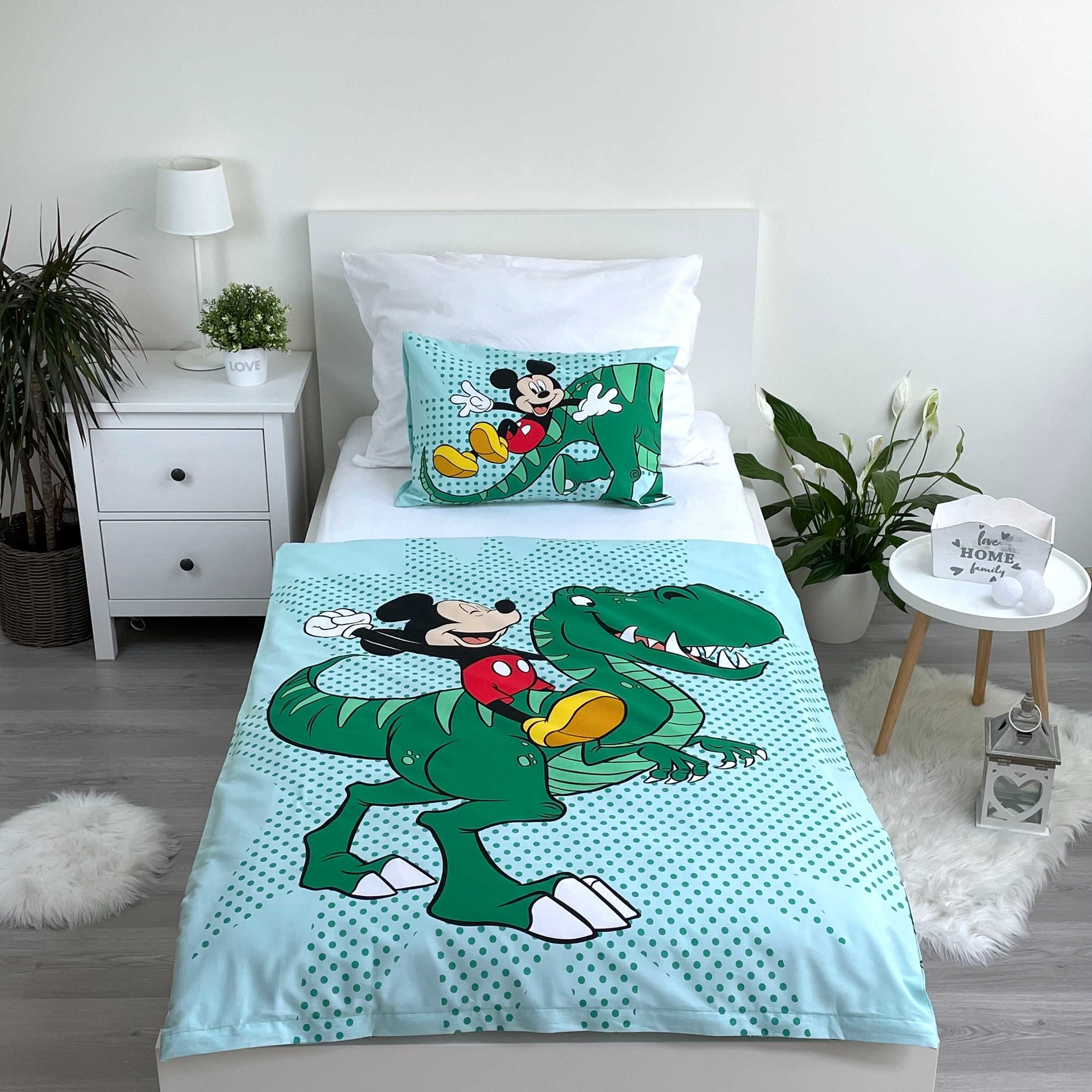Bettwäsche-Set mit Micky Maus und einem Dinosaurier. Ein weißer Nachttisch und eine Pflanze im Hintergrund.