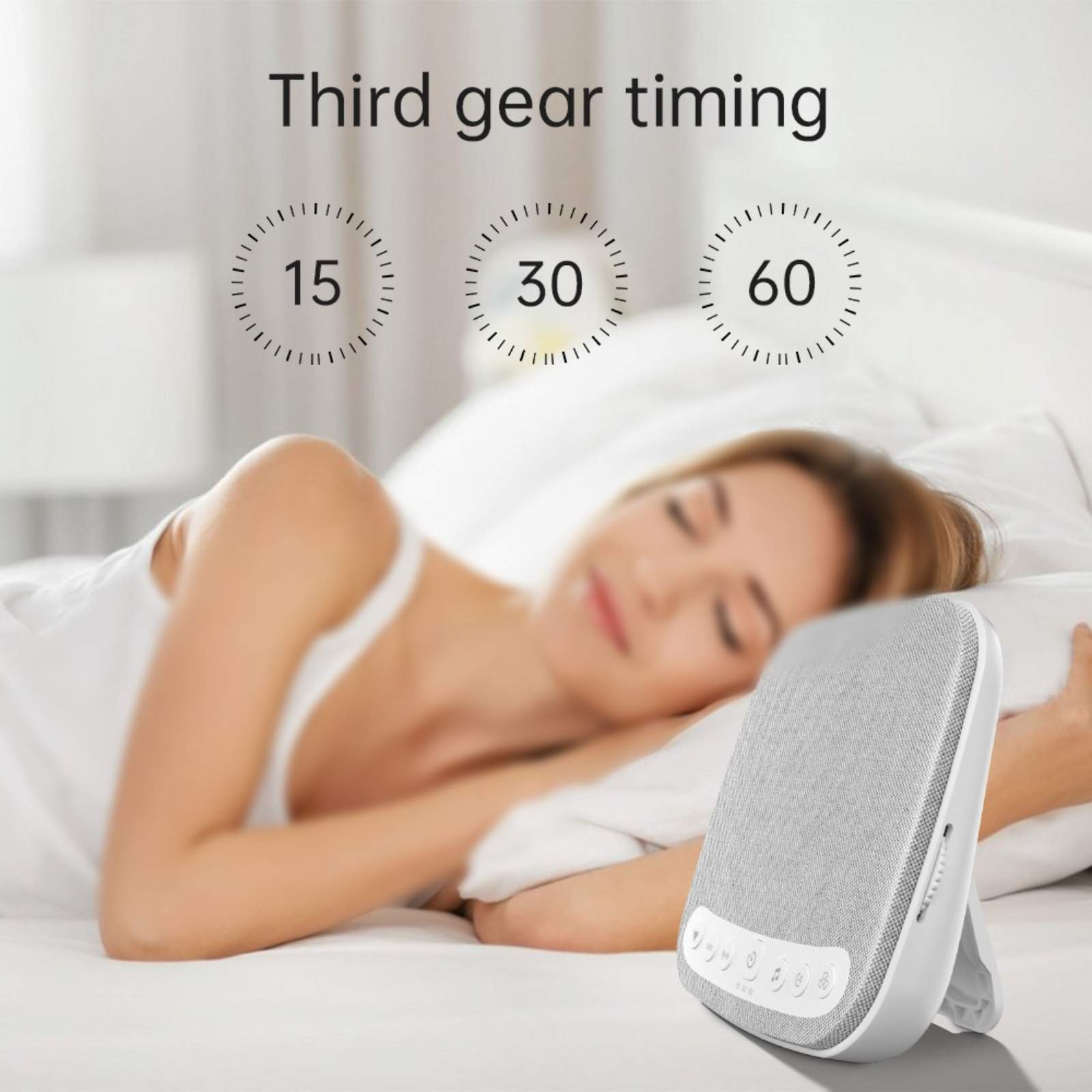 Eine Frau schläft im Bett mit einer Schlafgeräuschmaschine auf dem Nachttisch. Die Maschine hat ein weißes Design.