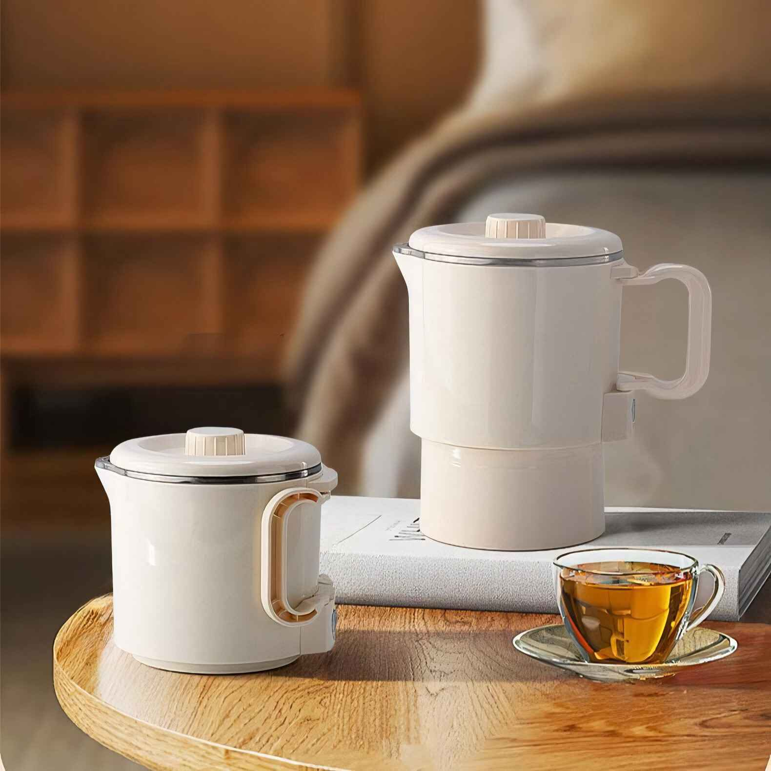 Zwei cremefarbene Teekannen und eine Tasse. Buch und ein Holztisch. Tee und Küchenutensilien.