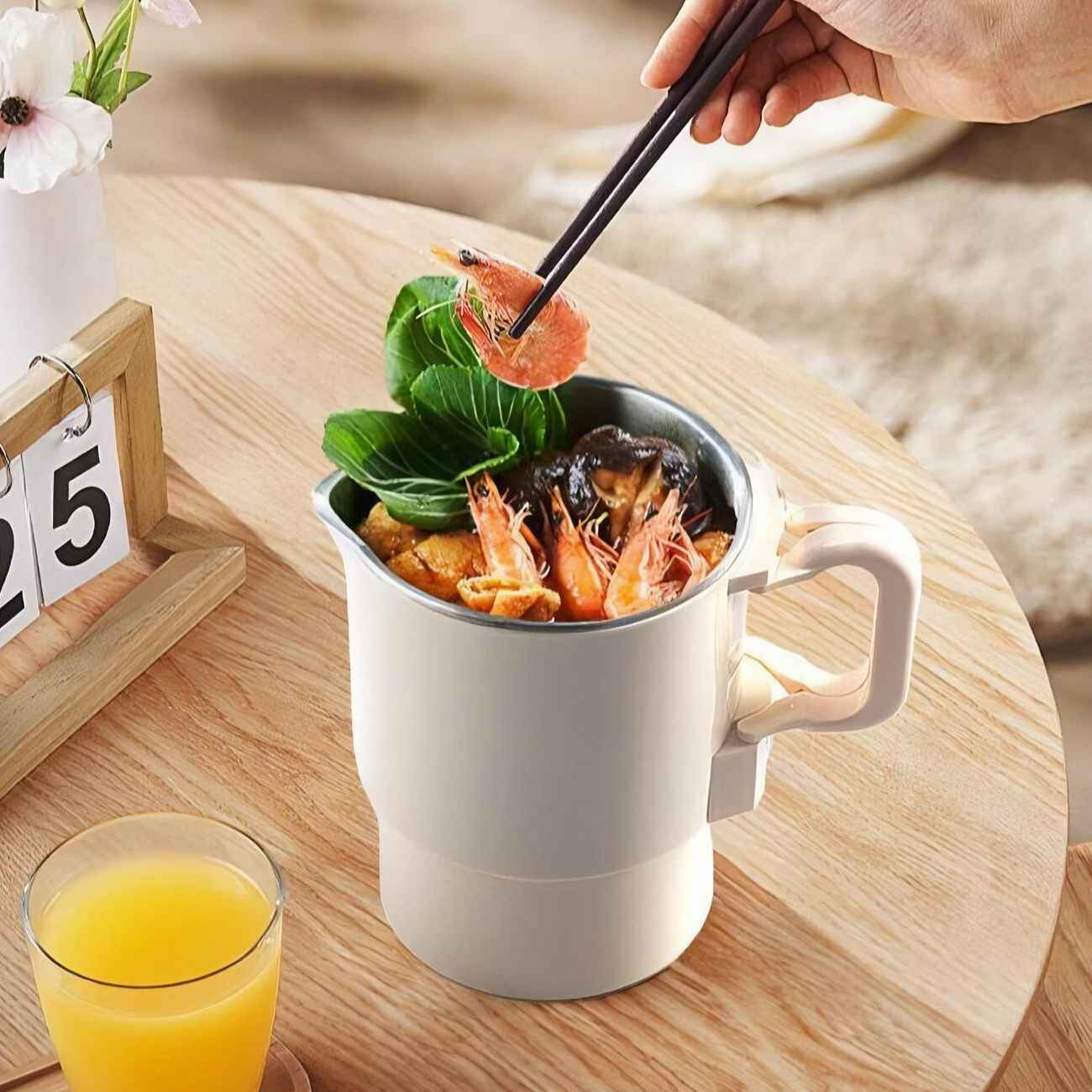 Eine Hand hält Essstäbchen mit einer Garnele über einem mit Essen gefüllten elektrischen Wasserkocher.
