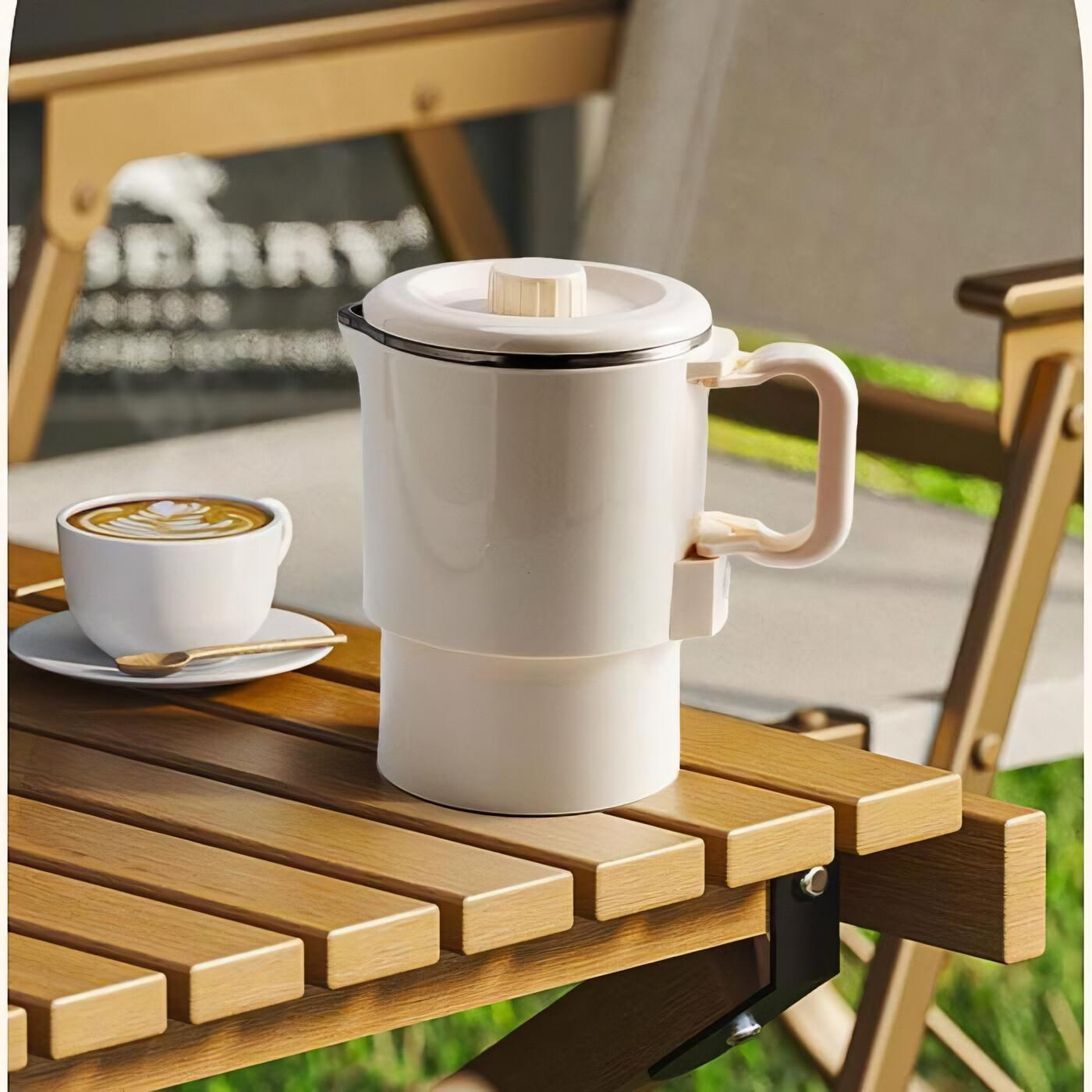 Weißer Reisekessel und eine Tasse Kaffee auf einem Holztisch. Im Hintergrund ein Klappstuhl.