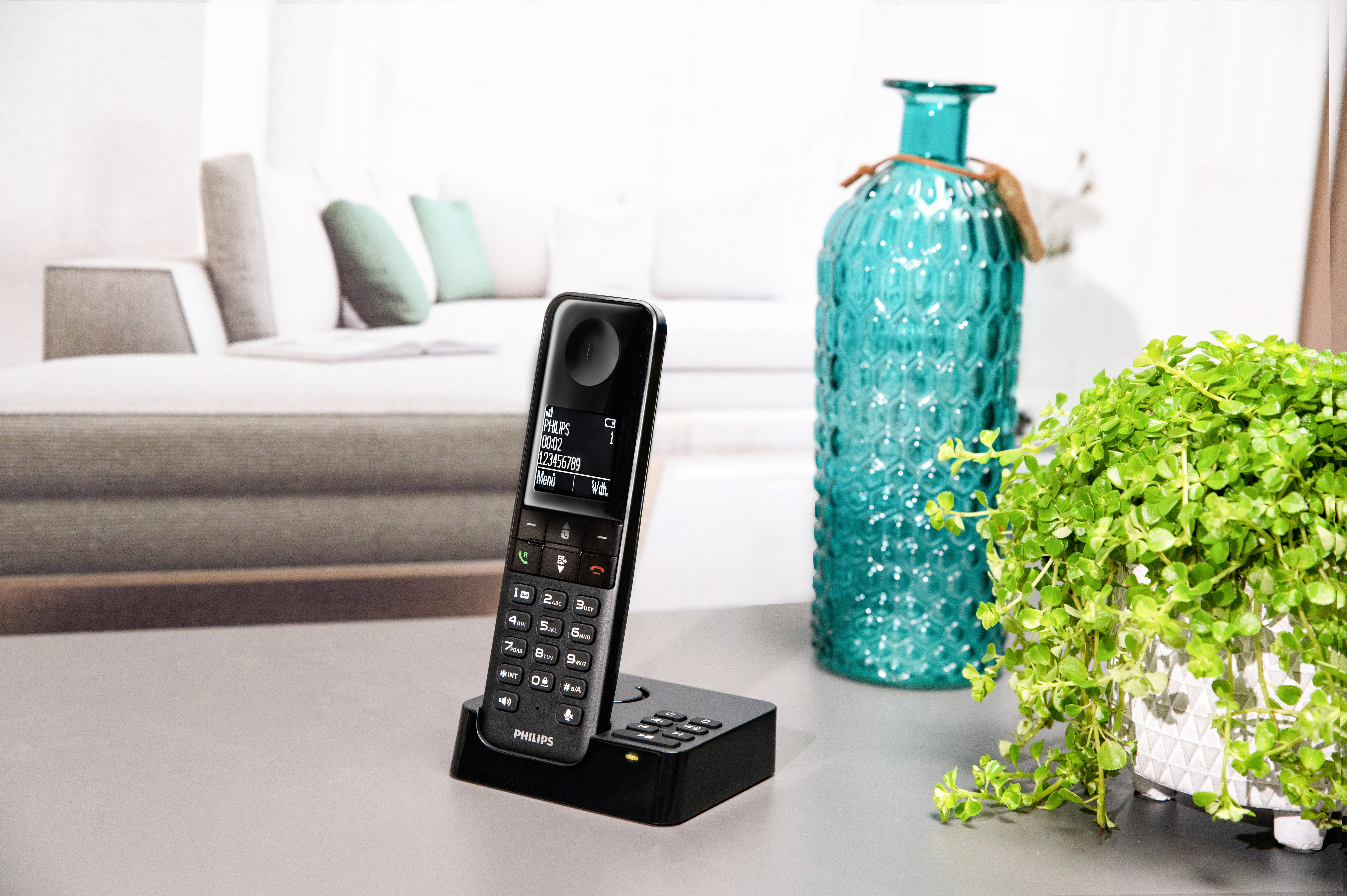 Un téléphone sans fil Philips noir sur une base de chargement, avec un écran affichant des chiffres, sur une table.