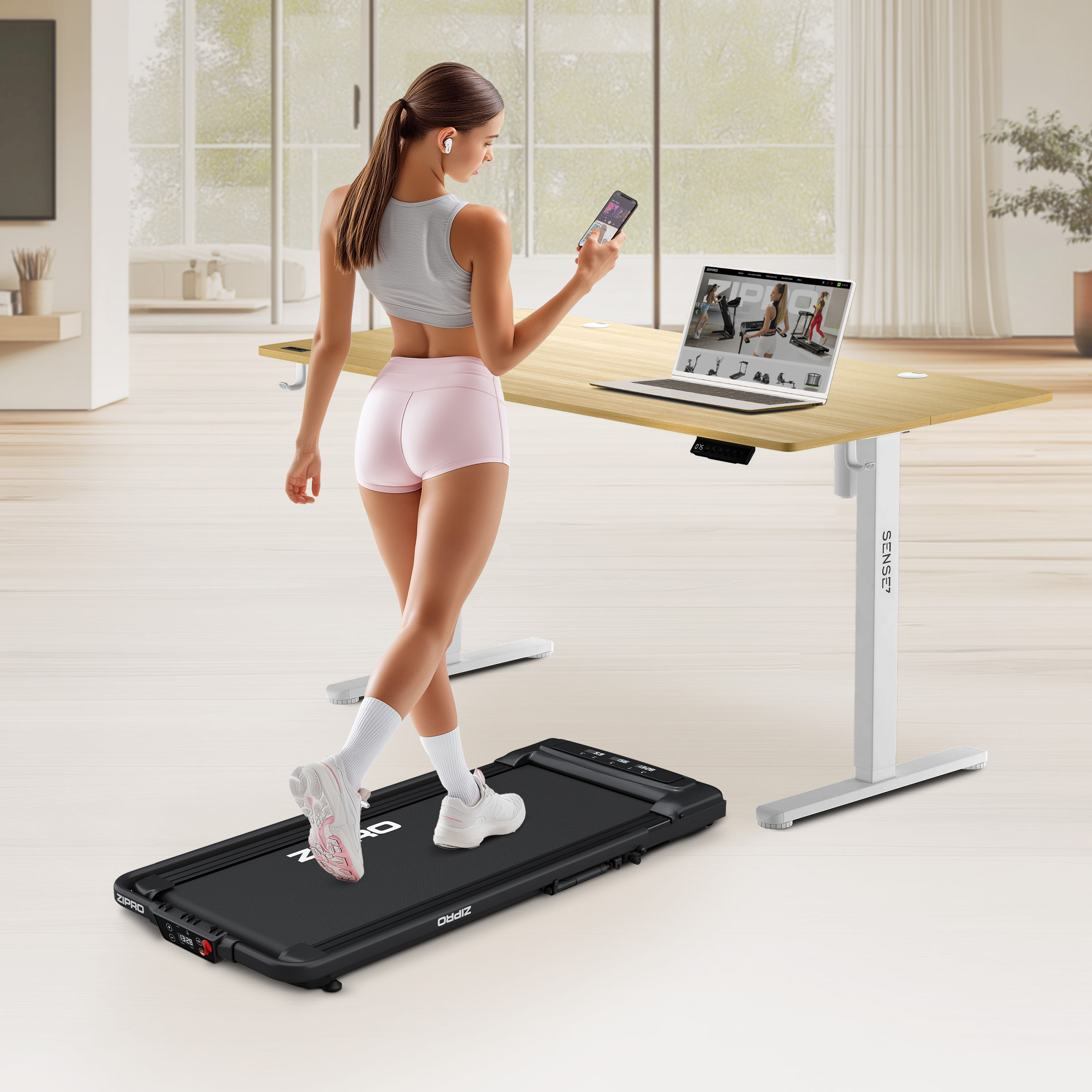 Frau geht auf einem Laufband, benutzt einen Laptop und hält ein Telefon. Schreibtisch sichtbar.