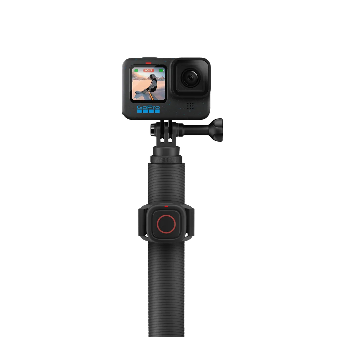 Eine GoPro-Kamera ist auf einem schwarzen Selfie-Stick montiert. Die Kamera zeigt eine Person beim Skifahren. Ein roter Kreisk Knopf ist sichtbar.