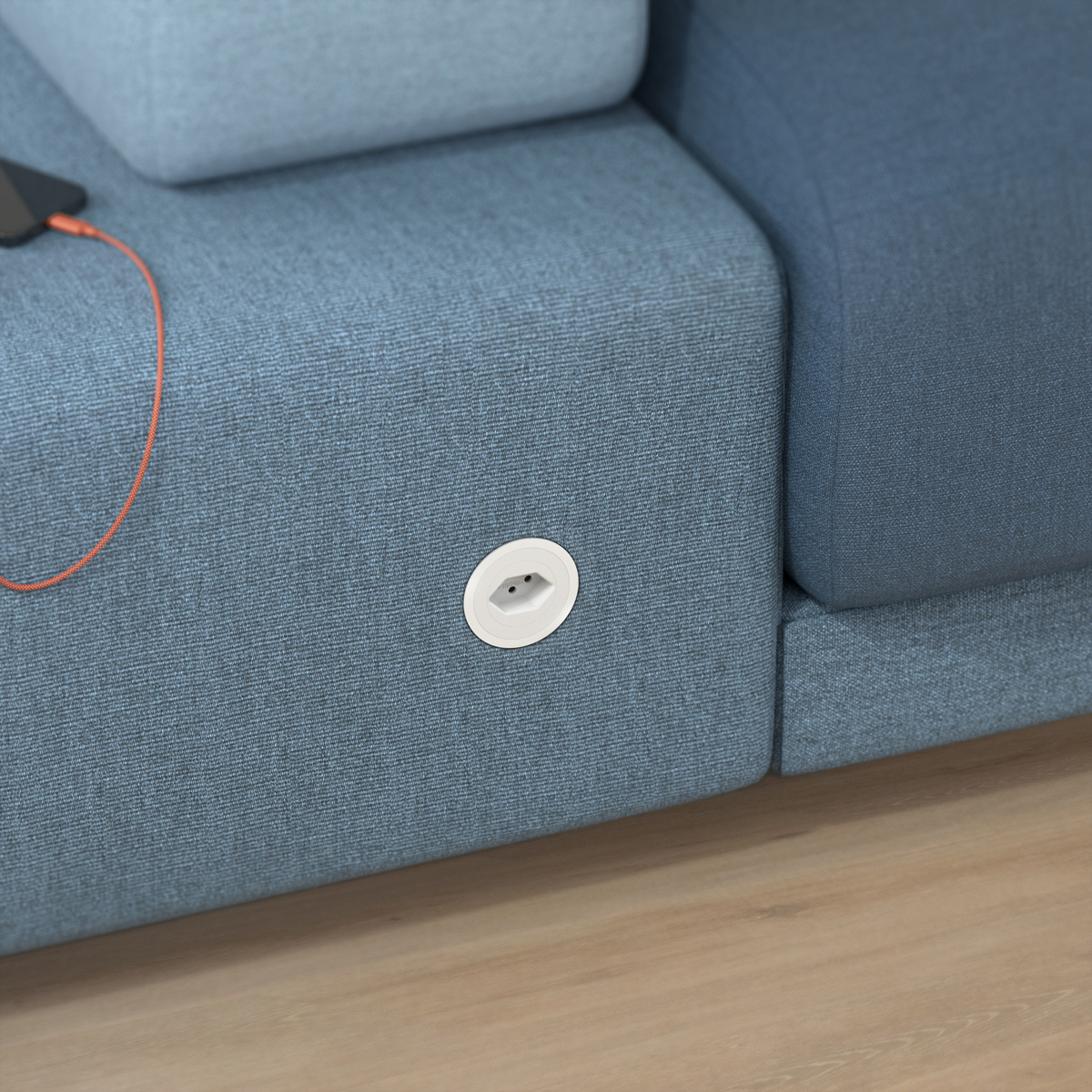 Niebieska sofa z wbudowanym gniazdkiem i telefonem ładującym się w pobliżu.