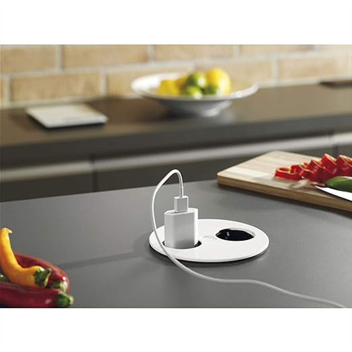 Plan de travail de cuisine avec un chargeur, des citrons, des poivrons et une planche à découper avec un couteau.