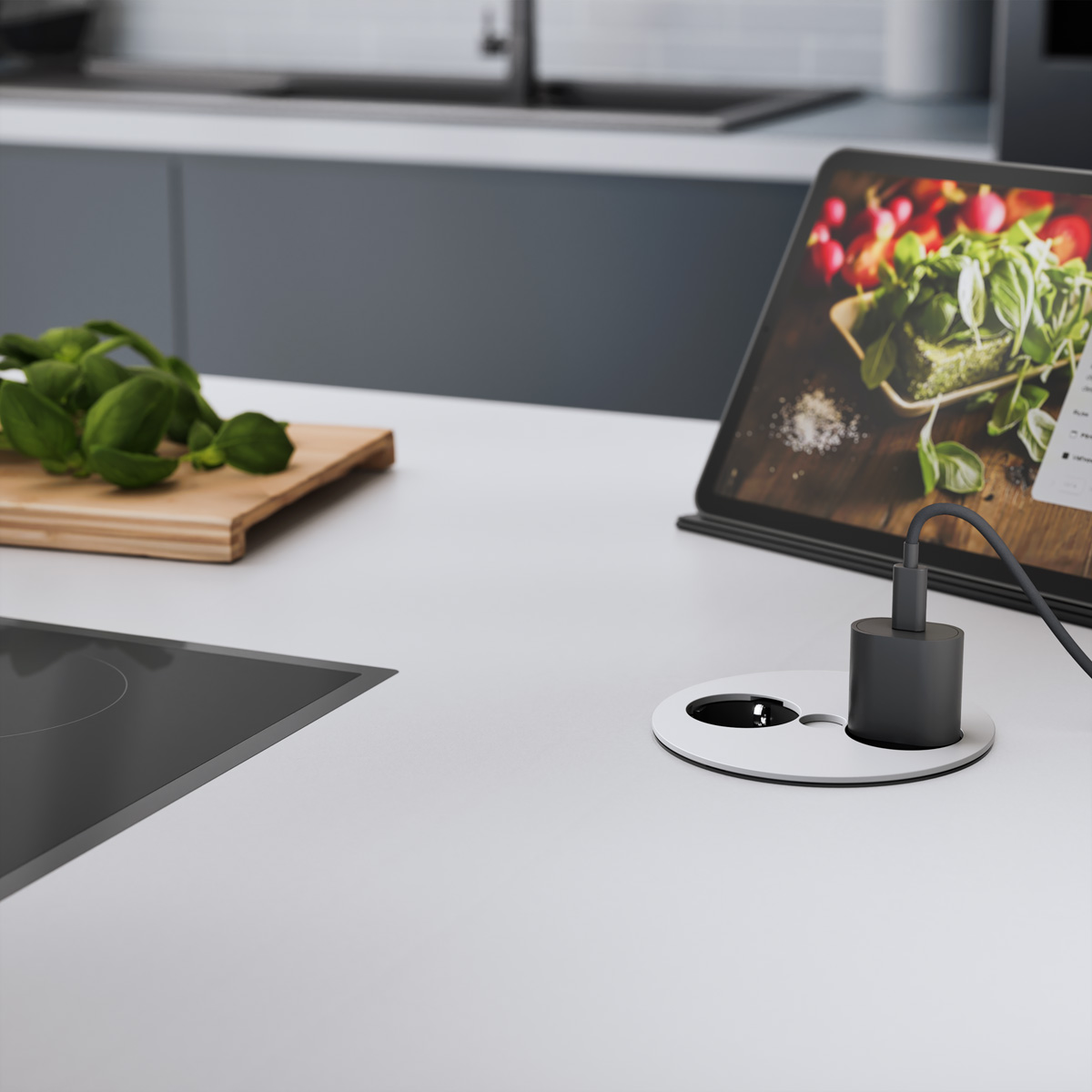 Piano cucina con tablet, basilico, tagliere e presa di corrente con caricatore.