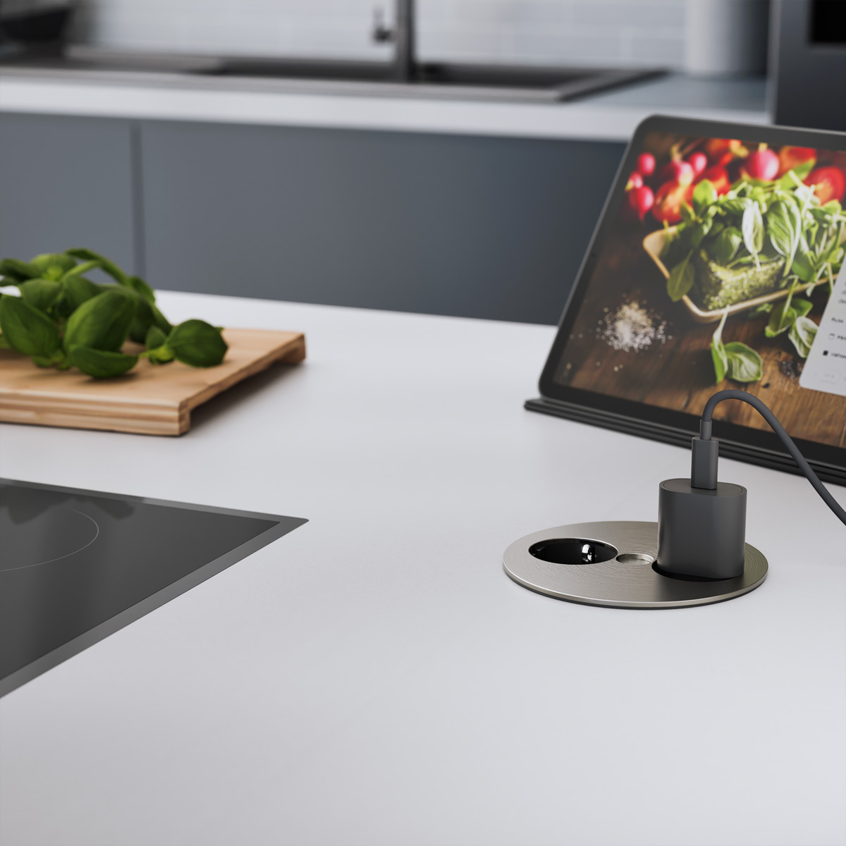 Blat kuchenny z tabletem, gniazdem, bazylią i deską do krojenia.