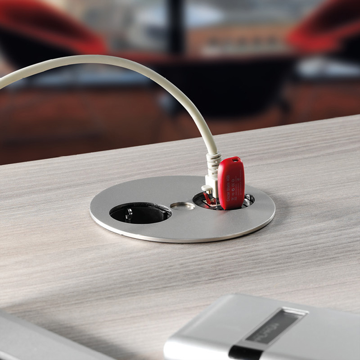 Una presa di corrente argentata con un dispositivo USB rosso collegato a un tavolo di legno.