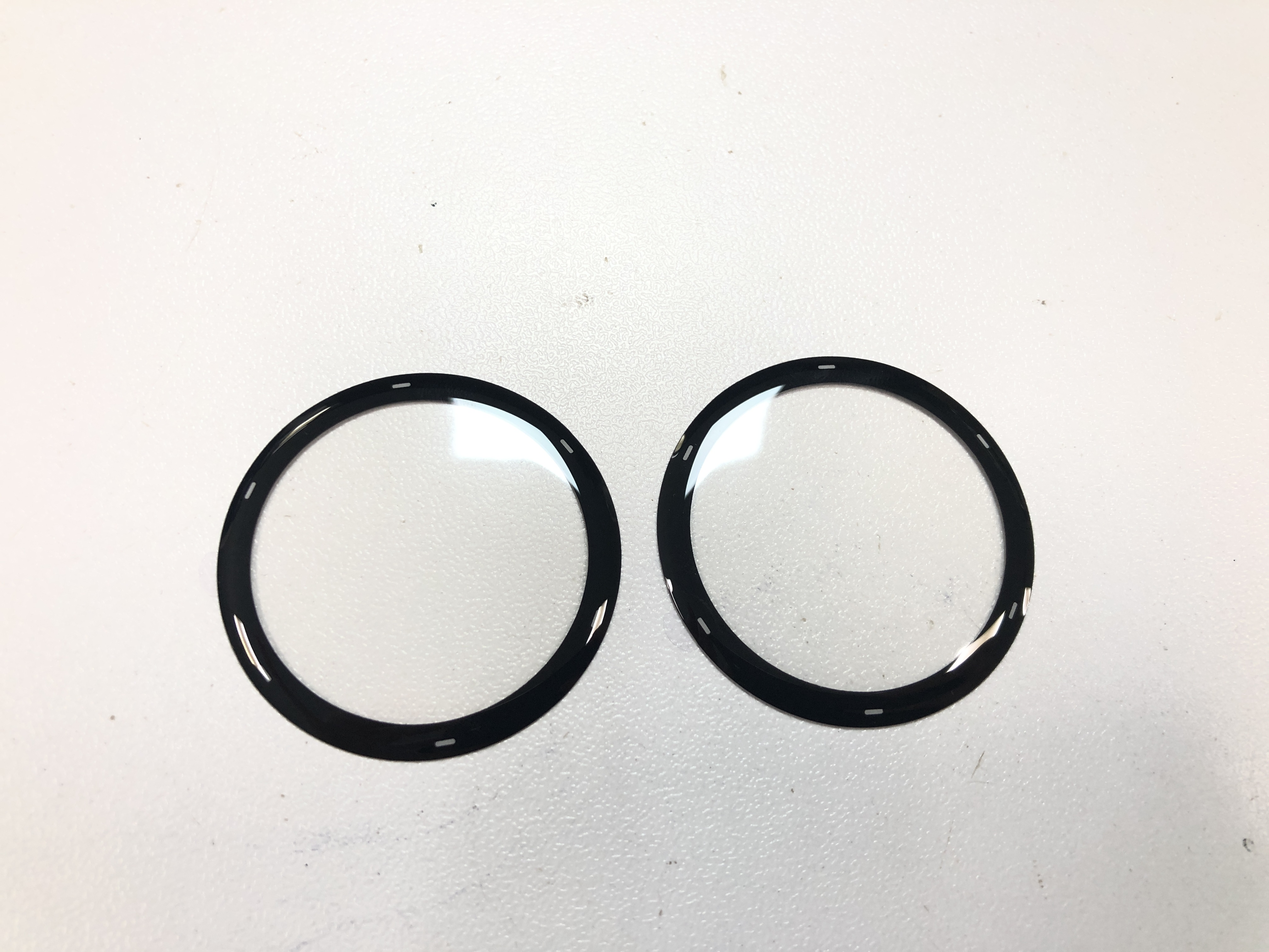 Dwie przezroczyste osłony ekranu do smartwatcha leżą płasko na białej powierzchni.