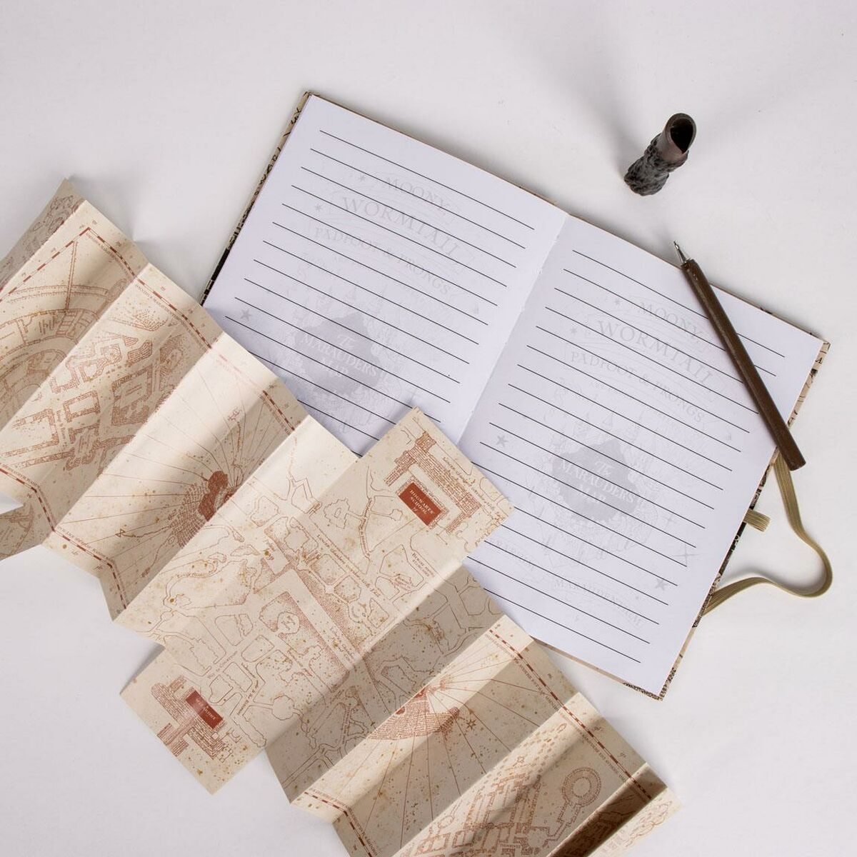 Offenes Notizbuch und Marauder's Map. Die Karte ist entfaltet und zeigt Zeichnungen. Ein Stift liegt daneben.