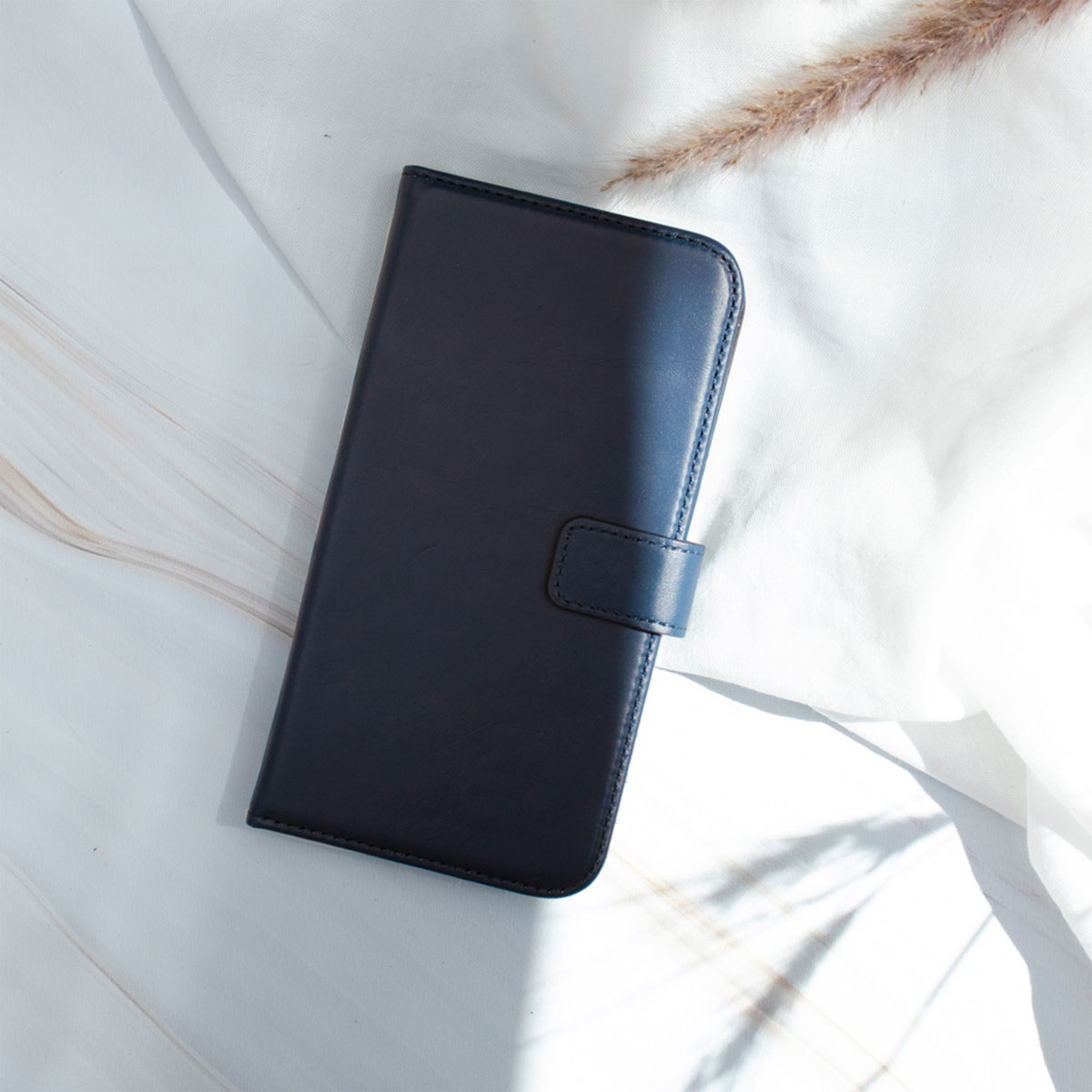Un étui de téléphone bleu fermé sur une surface blanche avec une tige de plante. L'étui a une fermeture magnétique.