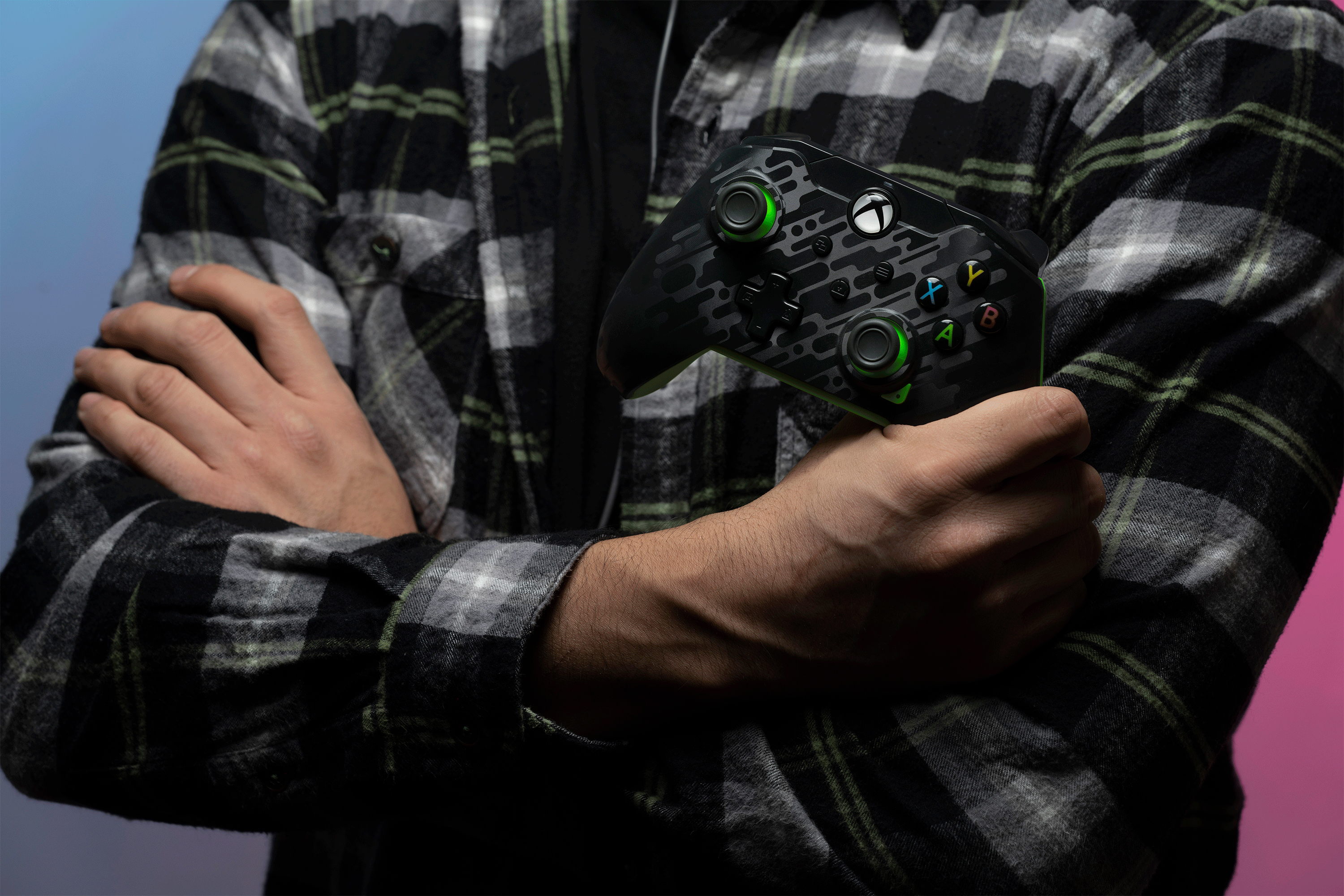 Una persona che tiene un controller Xbox. Il controller è nero con dettagli verdi e la persona indossa un plaid.