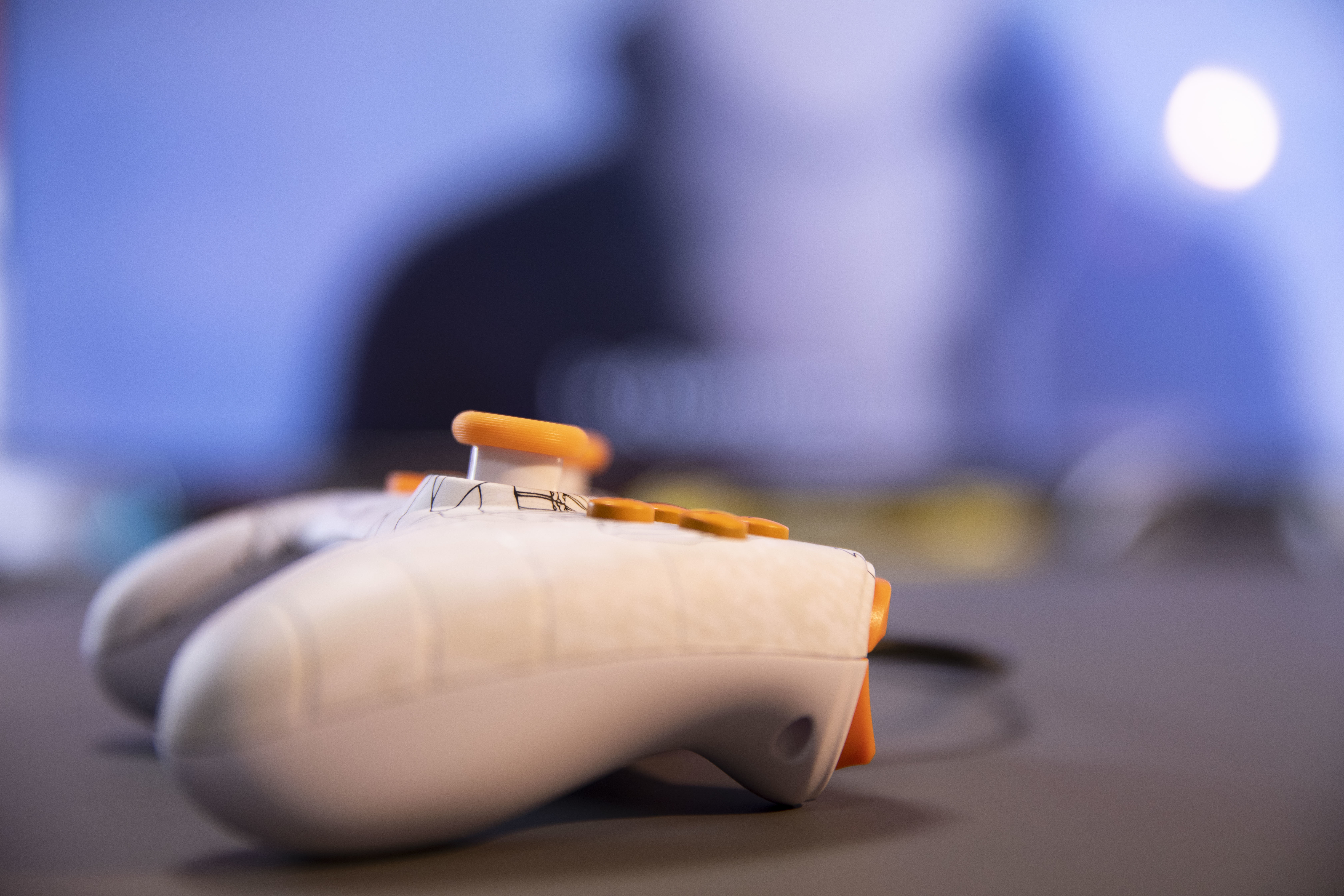 Dwa biało-pomarańczowe kontrolery na szarej powierzchni. Kontrolery są nieostre.