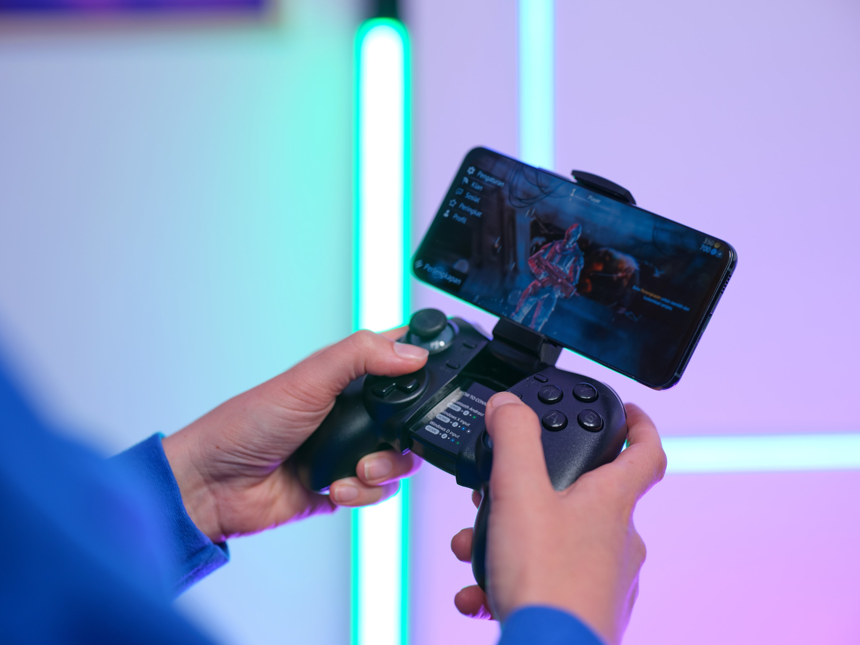 Mani che tengono un telefono cellulare con un gioco visualizzato. Controller di gioco collegato.