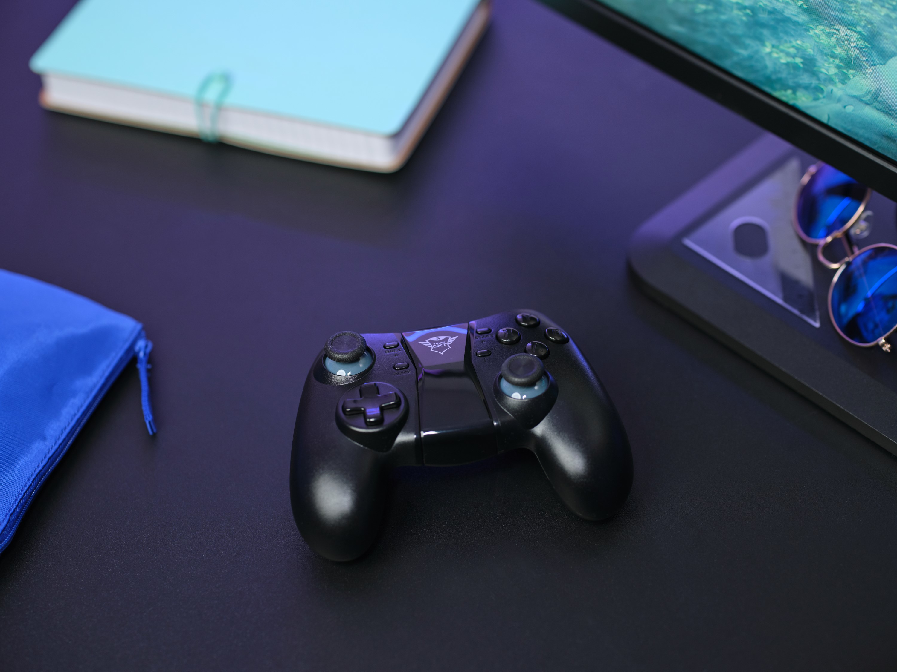 Controller nero su un tavolo nero. Sono presenti anche un taccuino, un monitor e occhiali da sole.
