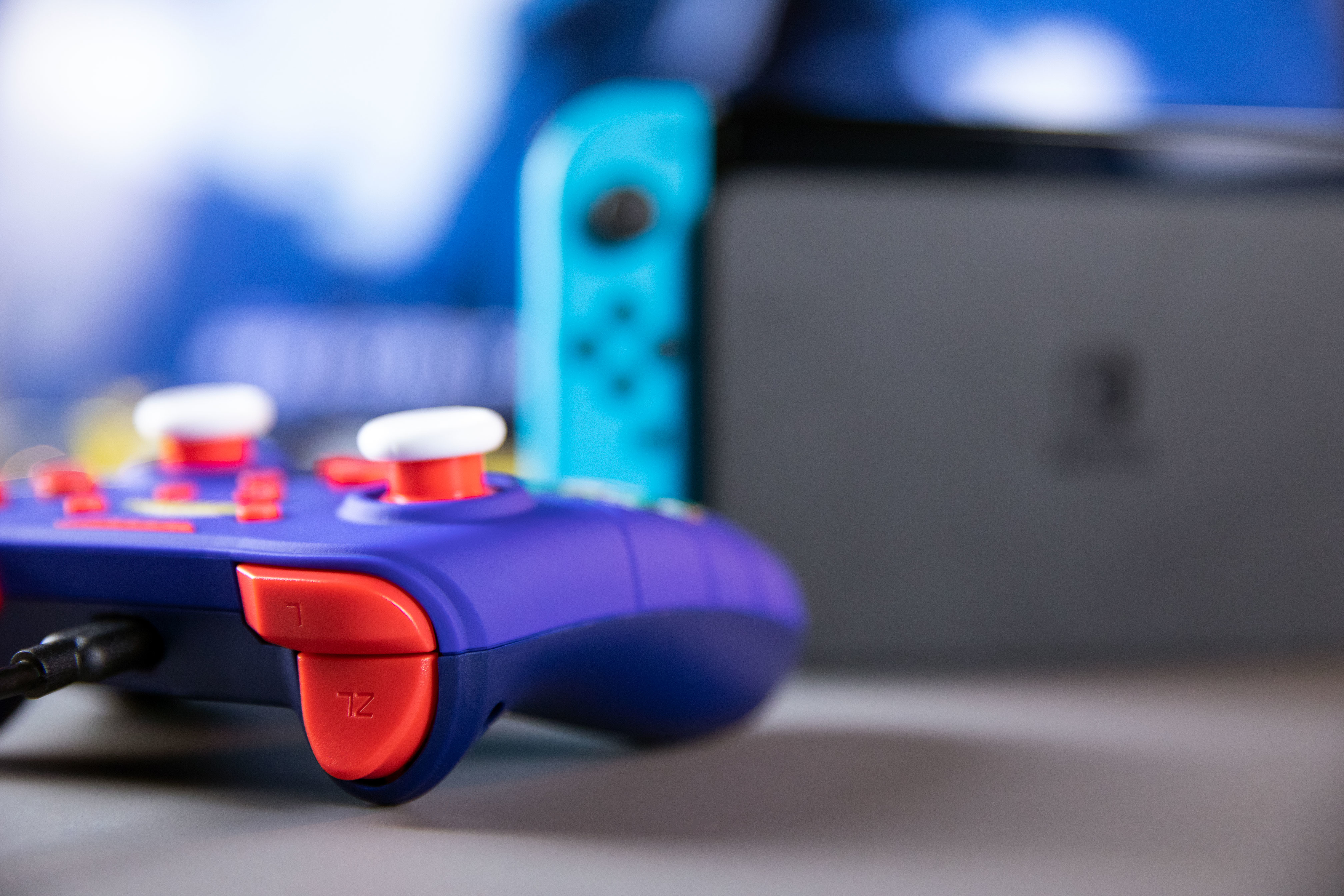 Controller blu, viola e rosso vicino a una TV, con un Joy-Con blu sullo sfondo.