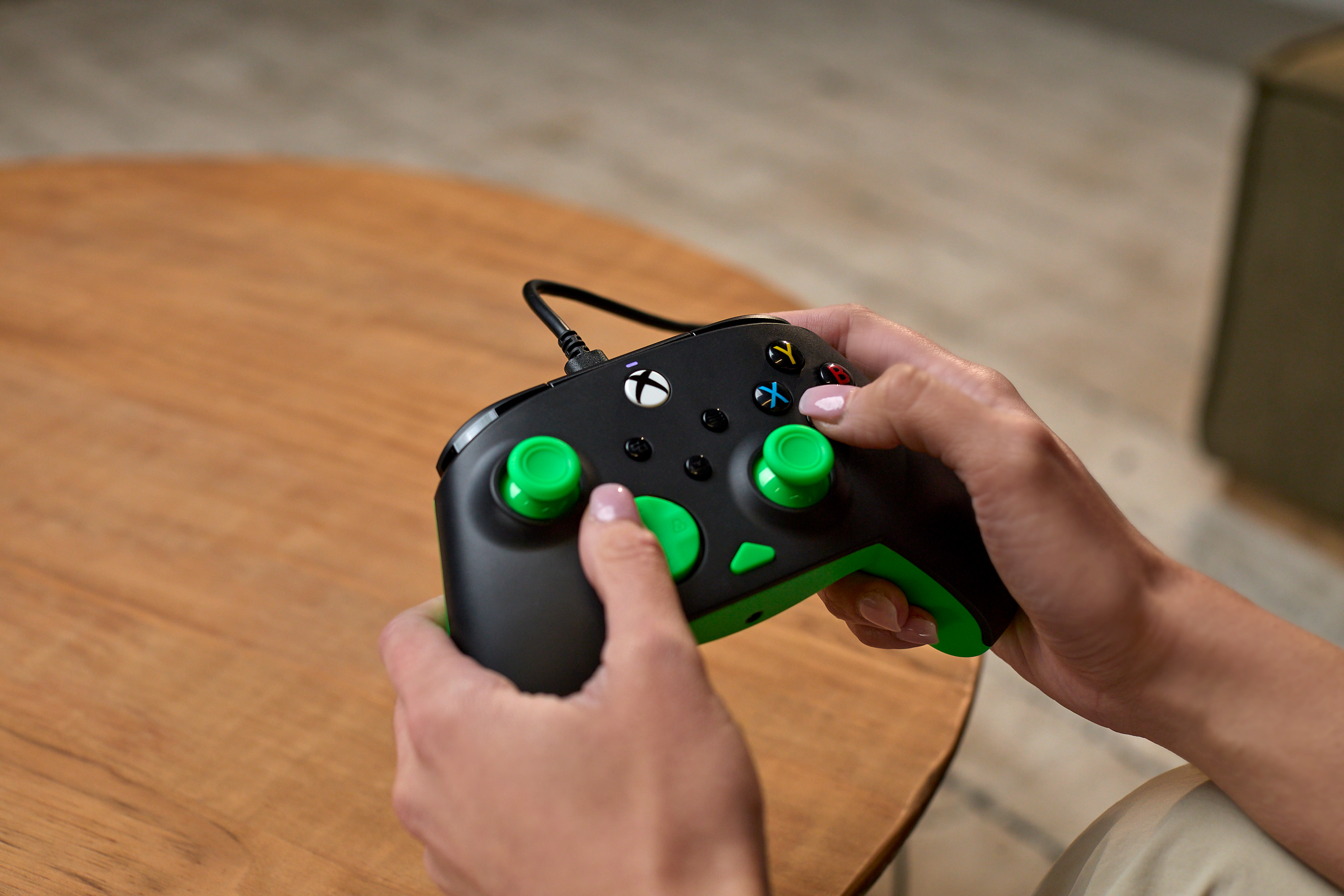 Une personne tient une manette noire et verte, posée sur une table en bois.
