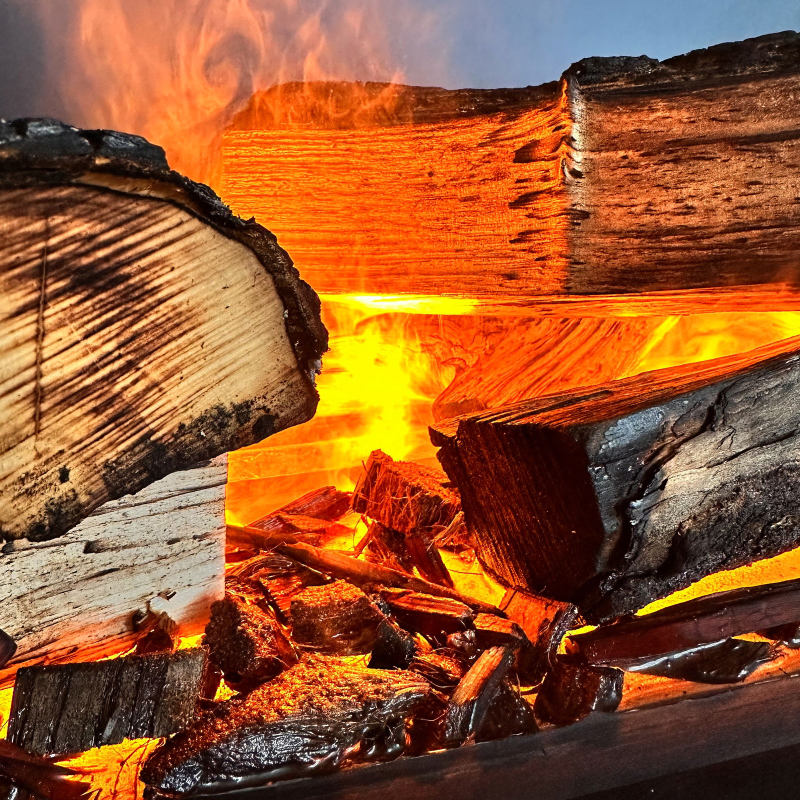 Nahaufnahme von brennenden Holzscheiten in einem Kamin, mit intensiven orangefarbenen Flammen und Glut.