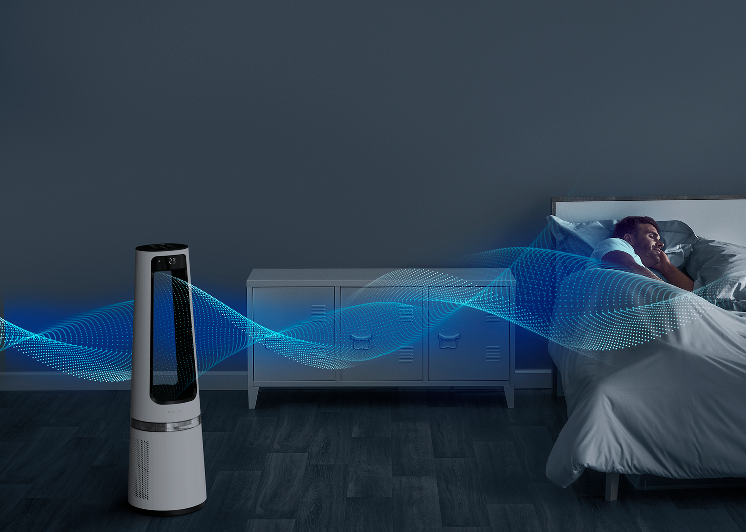 A man sleeps in bed with a fan blowing cool air. The fan is white and black.