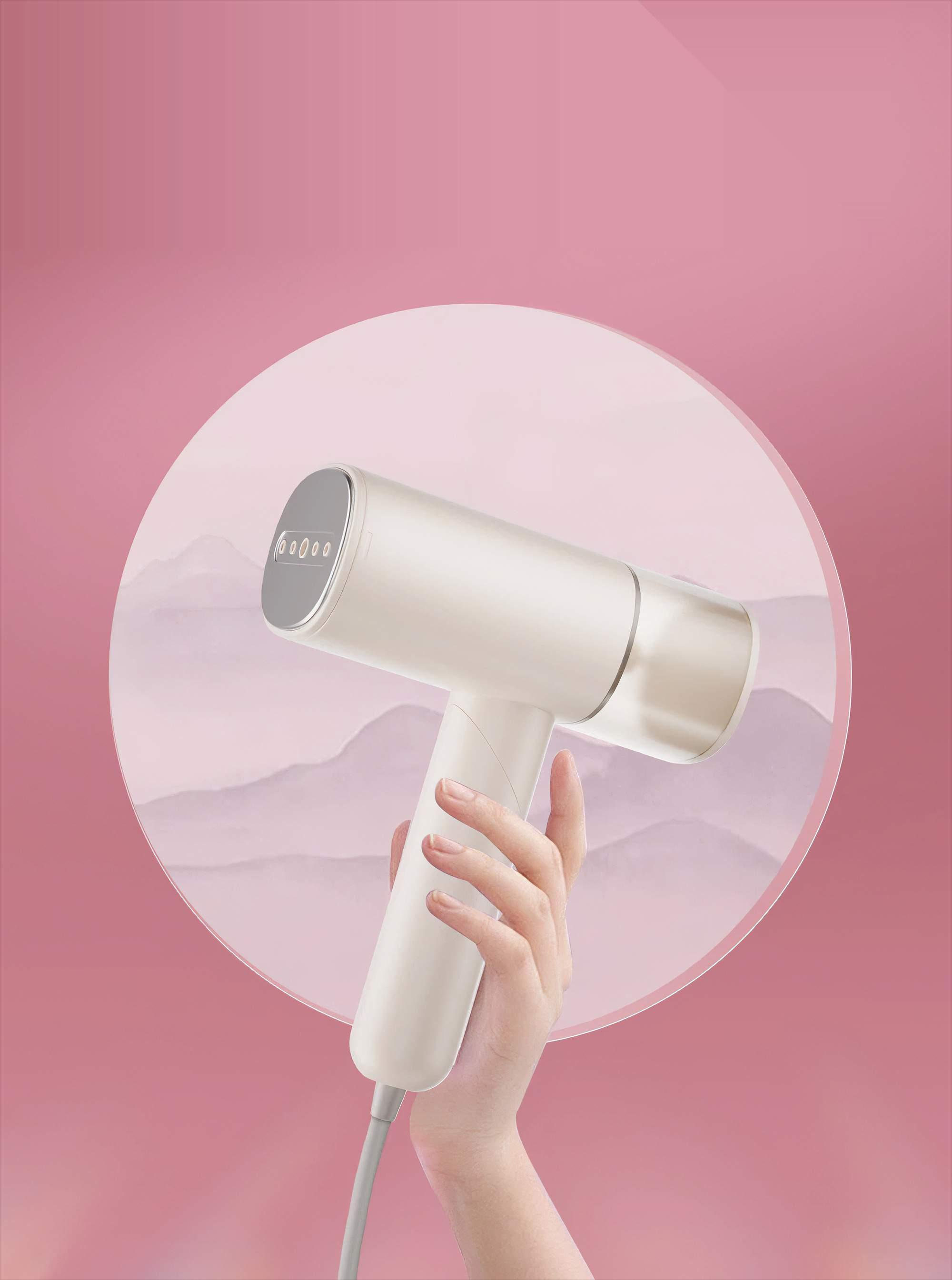 Ein Handdampfer, gehalten von einer Hand, vor rosa Hintergrund. Der Dampfer hat einen abgewinkelten Kopf.