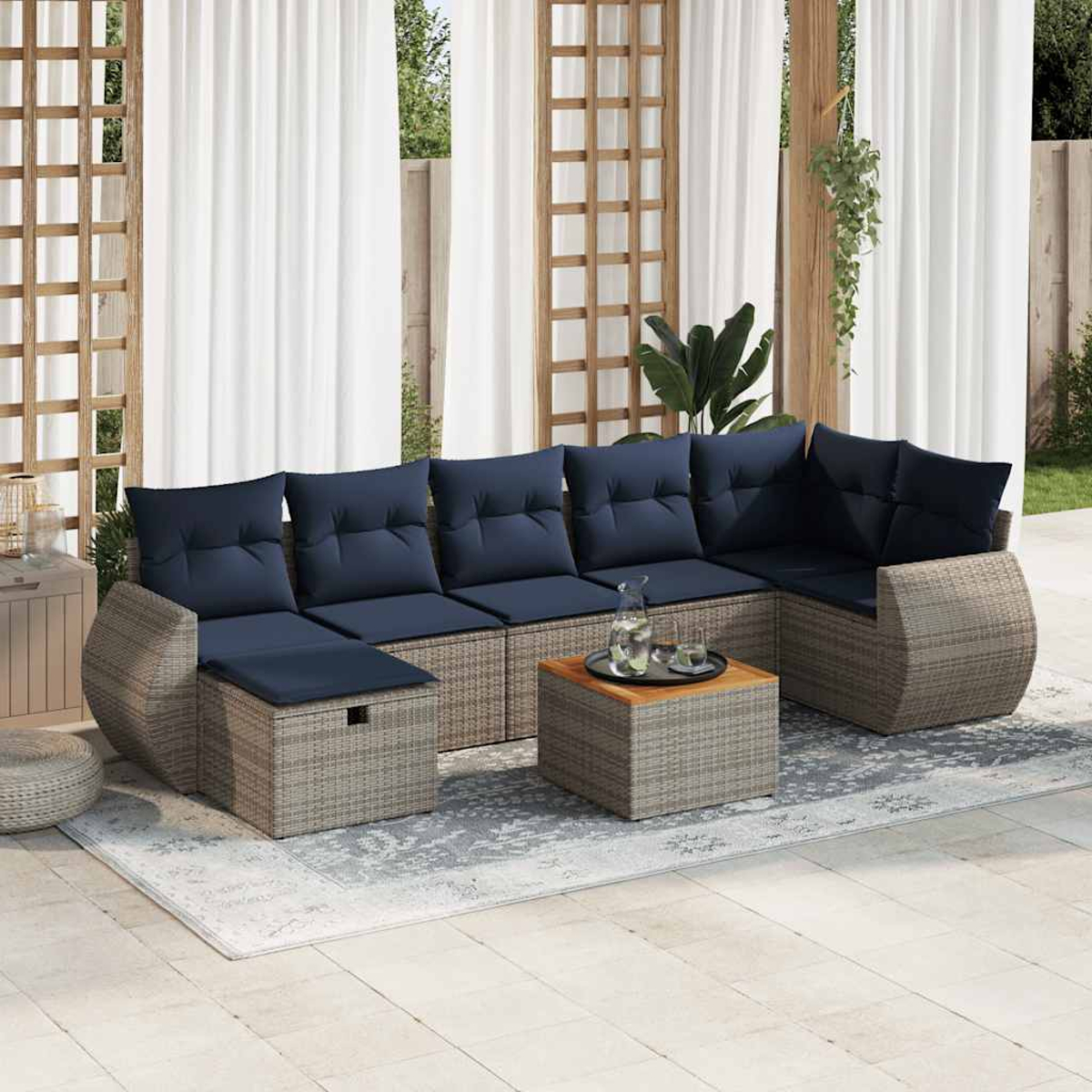 Ein Sitzbereich im Freien mit einem grauen Ecksofa aus Korbgeflecht, blauen Kissen und einem Holztisch.