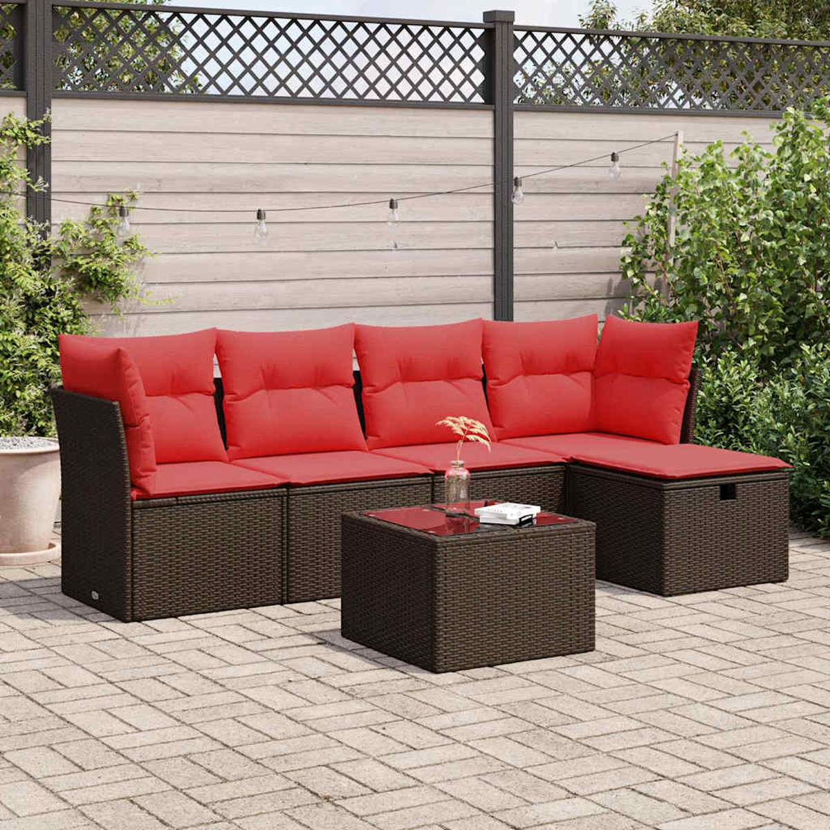 U-förmiges Rattansofa mit roten Kissen und einem Couchtisch. Die Kulisse ist eine Terrasse mit Zaun und Pflanzen.