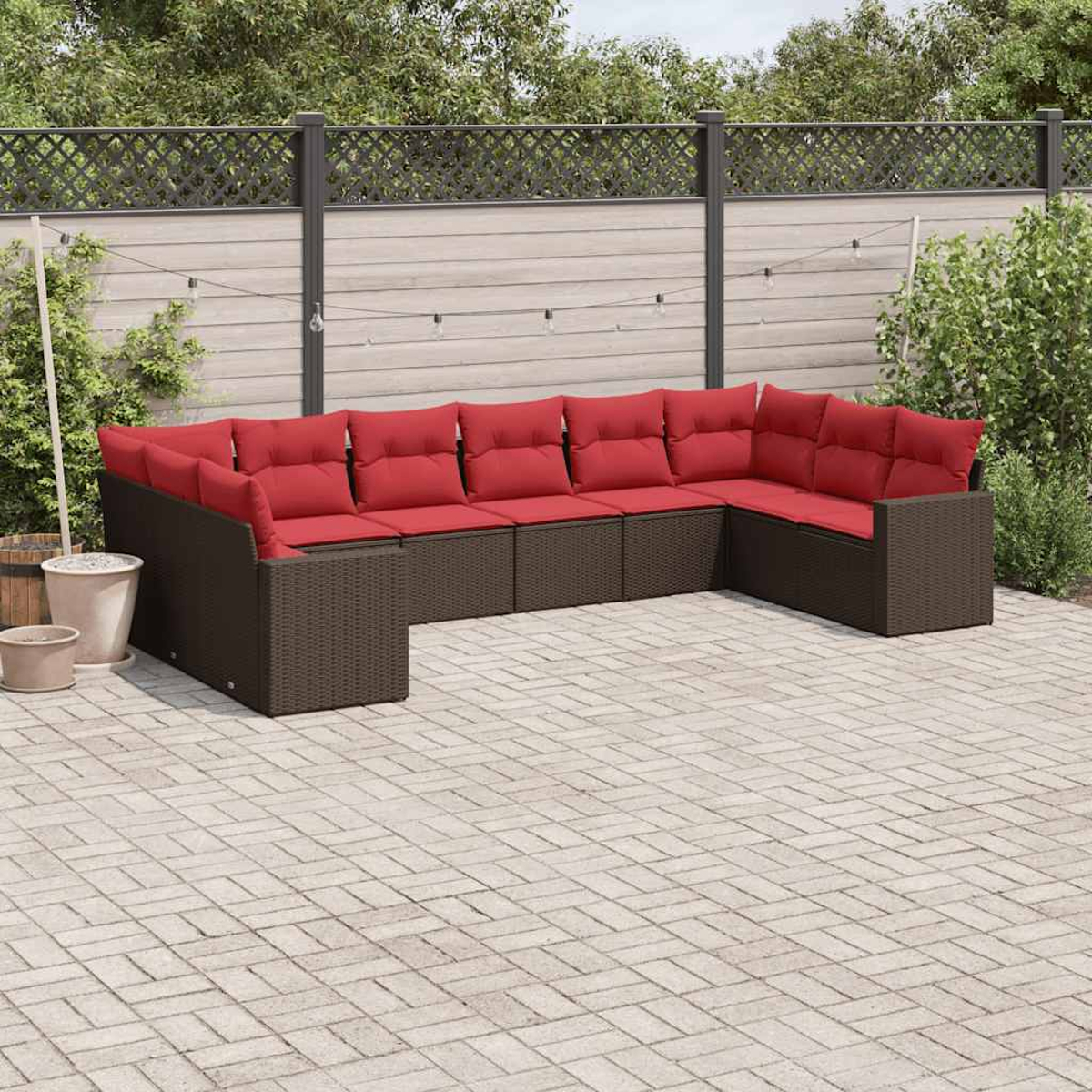 Dunkelbraunes U-förmiges Ecksofa aus Rattan mit roten Kissen auf einer Terrasse. Zaun und Pflanzen sichtbar.