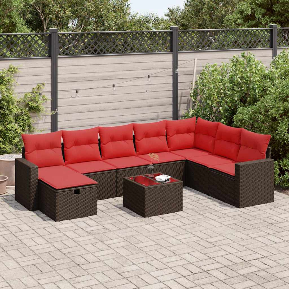 Eine braune Terrassengarnitur aus Korbgeflecht mit roten Kissen steht auf einer Ziegelterrasse und lädt zum Entspannen im Freien ein.