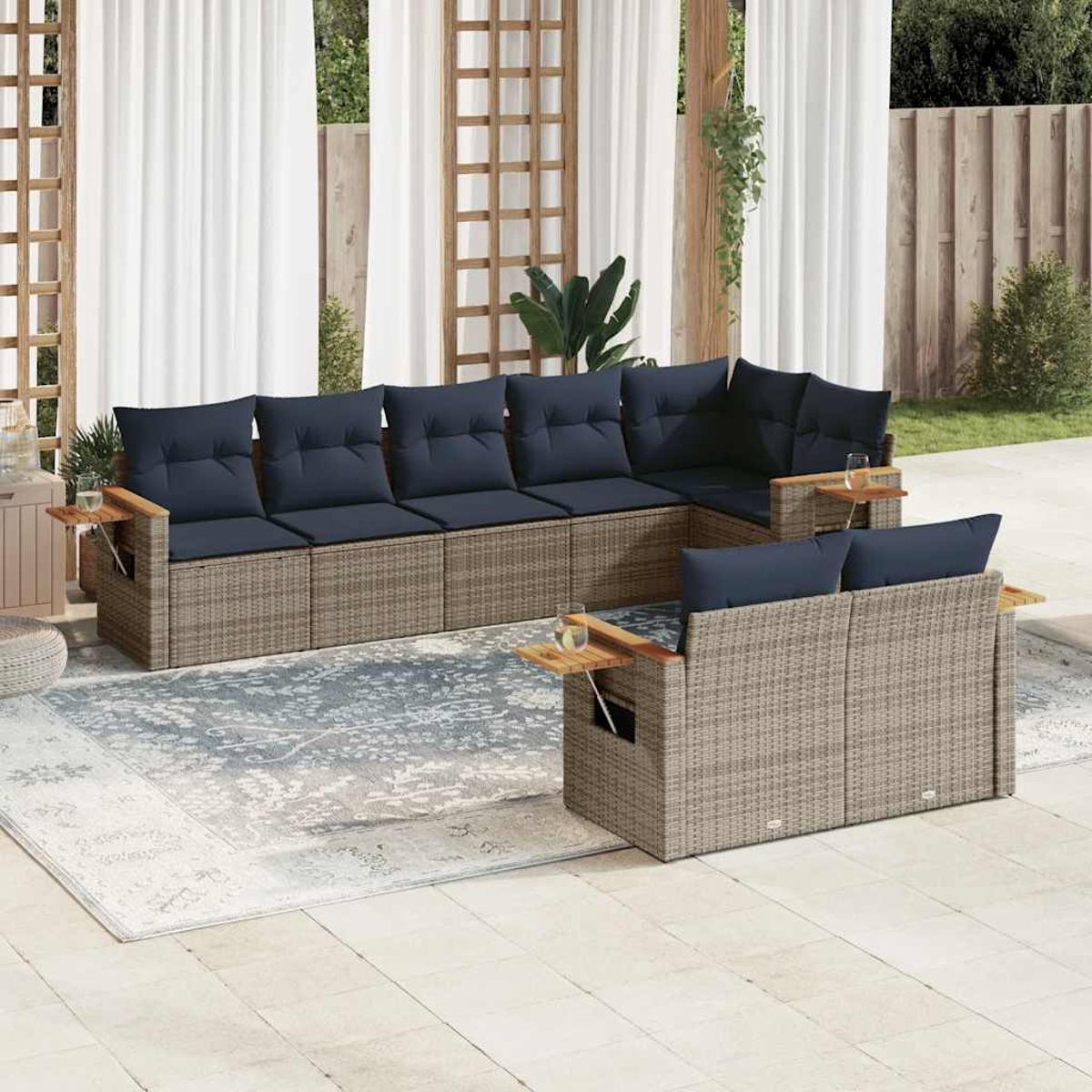 Rattansofa-Set mit marineblauen Kissen, Beistelltischen, auf einer Terrasse. Weiße Vorhänge im Hintergrund.