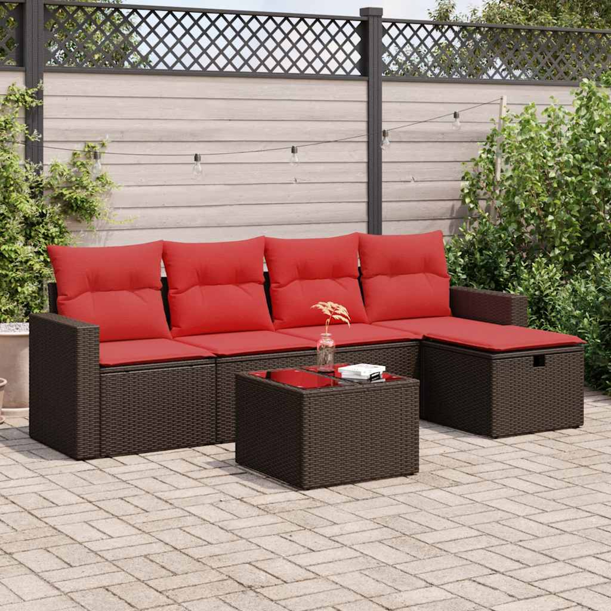 Terrassengarnitur im Freien mit dunkelbraunem Korbsessel und roten Kissen. Quadratischer Tisch davor, Ziegelterrasse.