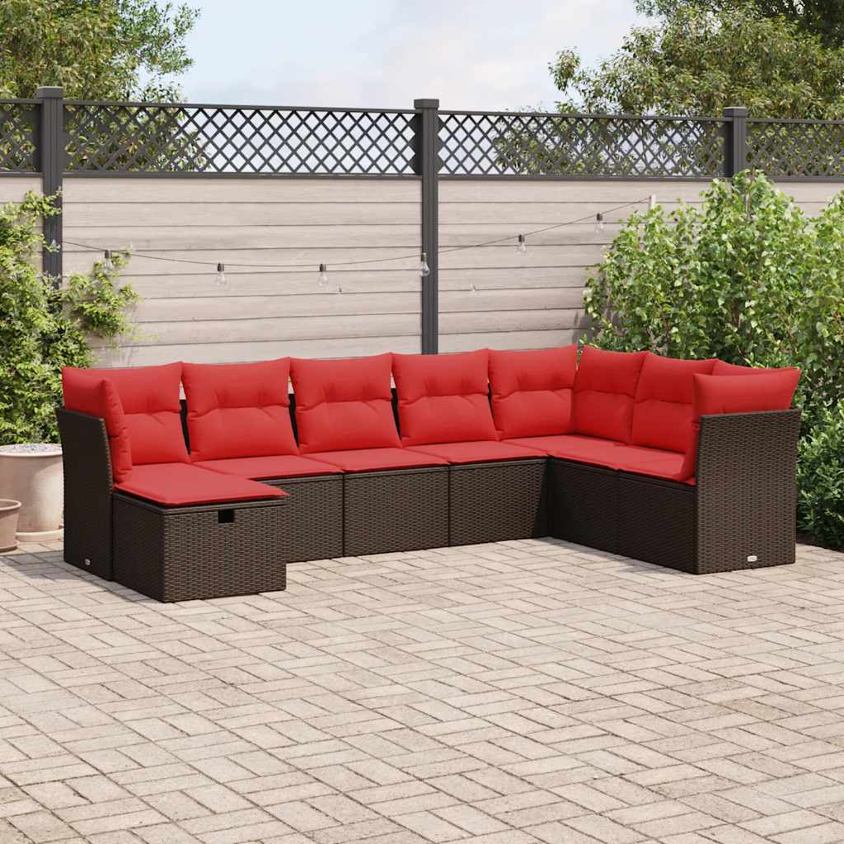 Ein Outdoor-Ecksofa mit braunem Korbgeflecht, roten Kissen, auf einer Ziegelterrasse. Im Hintergrund ein Zaun.
