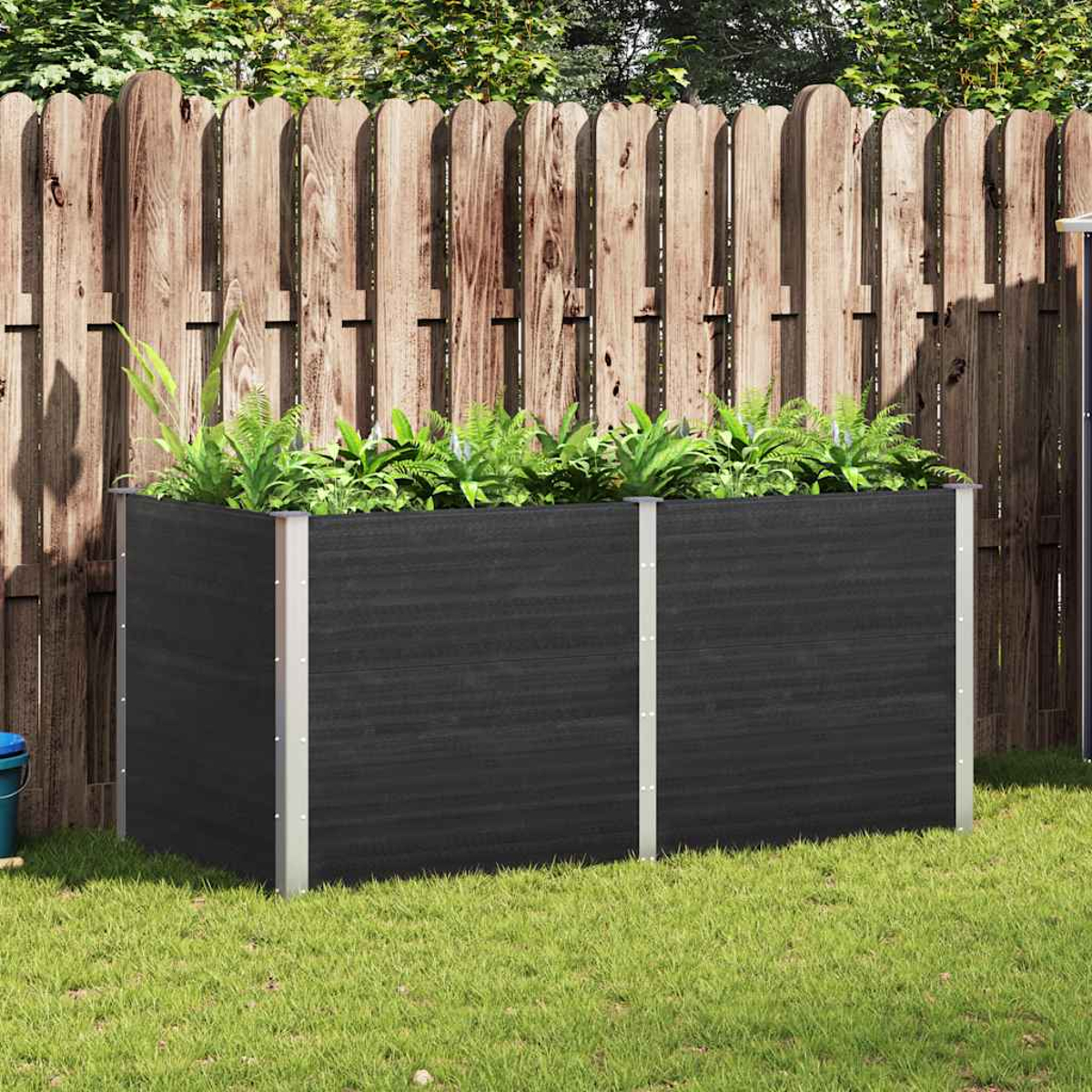 Ein erhöhtes Gartenbeet mit Pflanzen, auf Gras gesetzt, mit Holzzaun im Hintergrund.