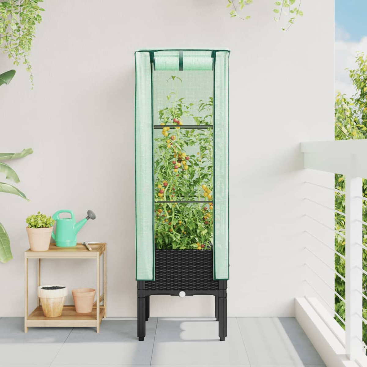 Un contenitore alto, ricoperto di verde, con piante di pomodoro. È su un balcone con altre piante e un annaffiatoio.