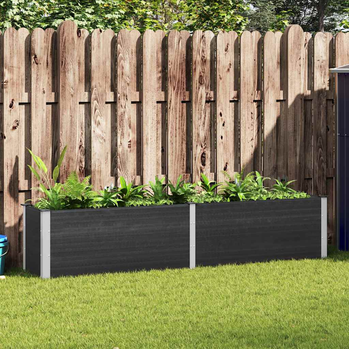 Zwei schwarze rechteckige Pflanzgefäße mit Pflanzen darin, vor einem Holzzaun. Grünes Gras sichtbar.