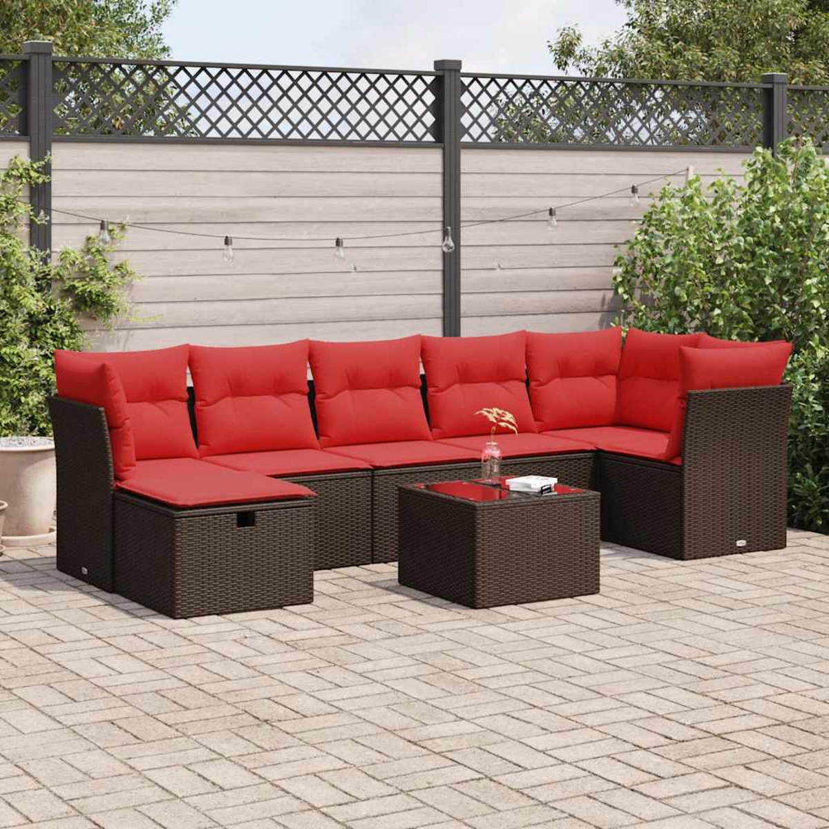 Ein Outdoor-Ecksofa mit roten Kissen. Es steht auf einer Backsteinterrasse mit schwarzem Zaun im Hintergrund.