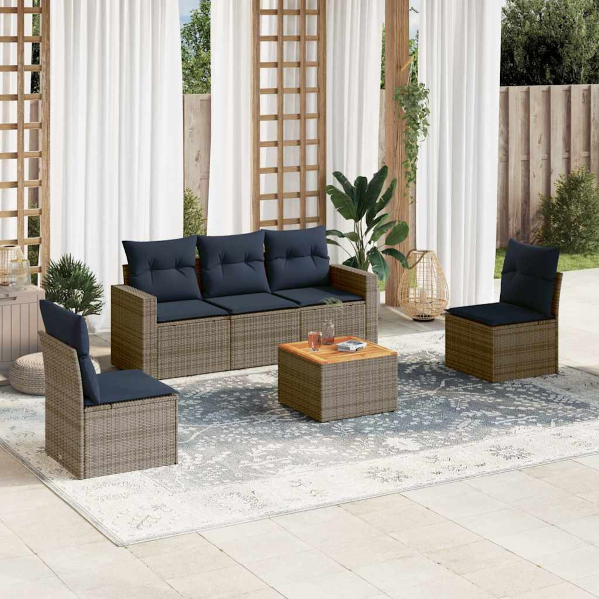 Juego de muebles de exterior con sofá, dos sillones y una mesa de centro. Mimbre gris, cojines azules y alfombra.